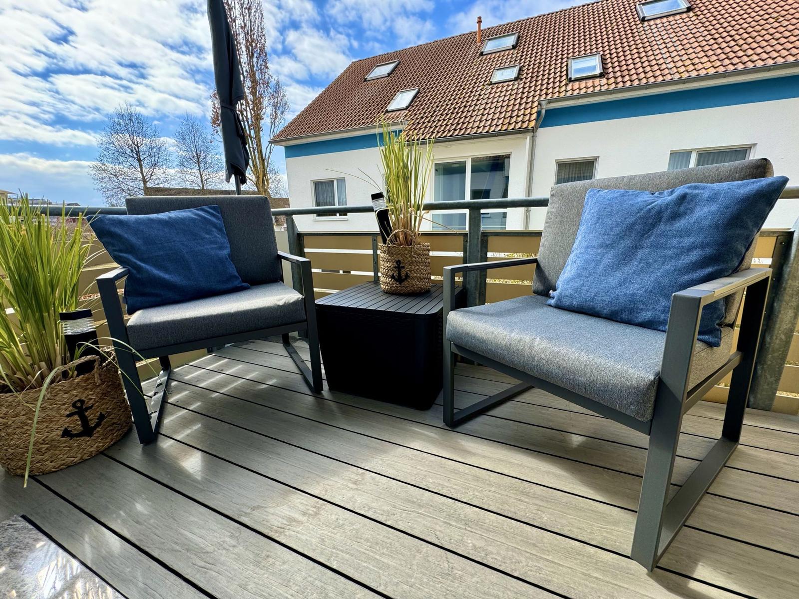 Terrasse mit zwei Sitzgelegenheiten und Pflanzen. Hintergrund: Haus mit Dachfenstern.
