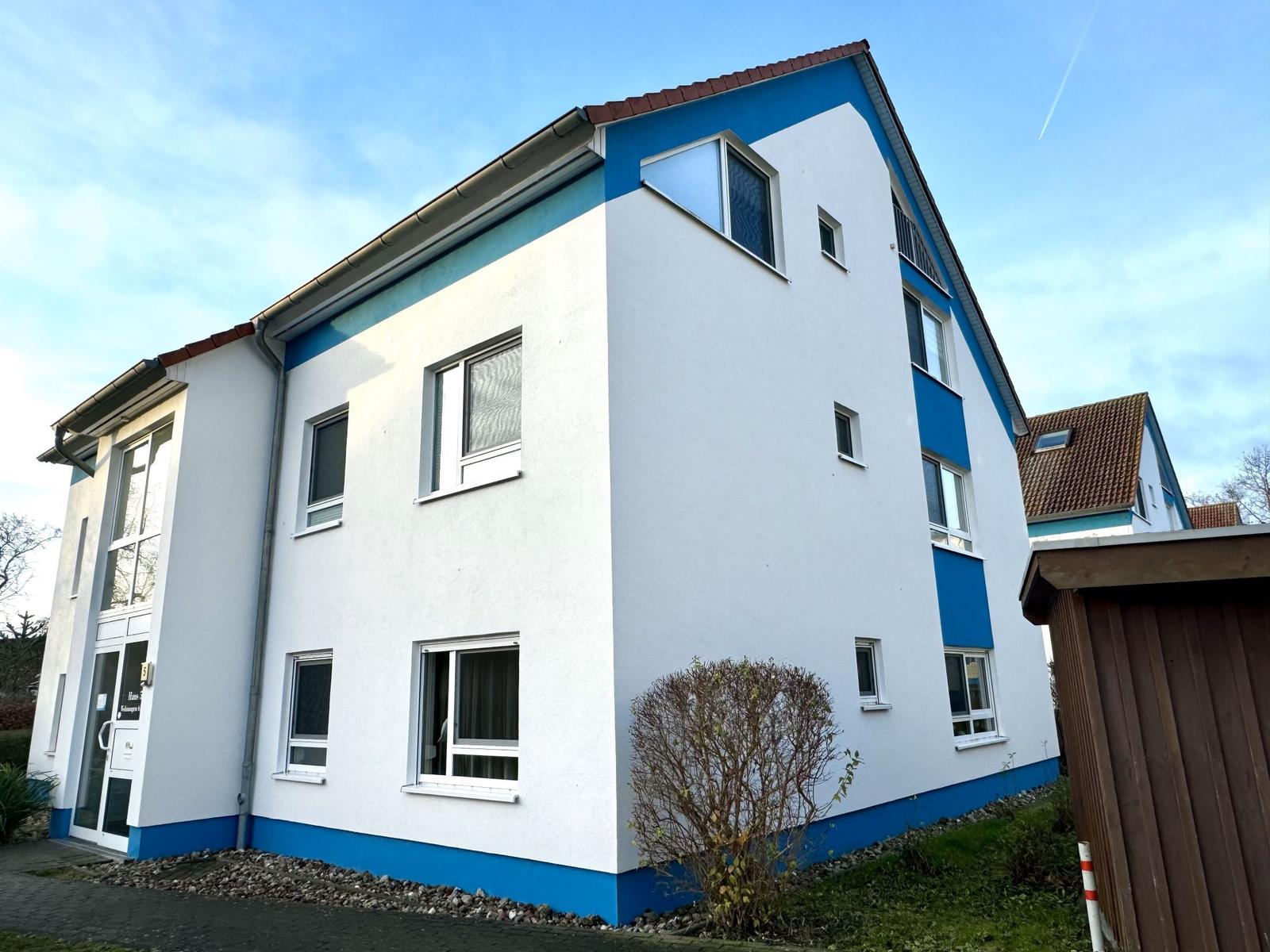 Zweistöckiges Haus mit weißen Wänden und blauen Akzenten. Viele Fenster und eine Eingangstür.