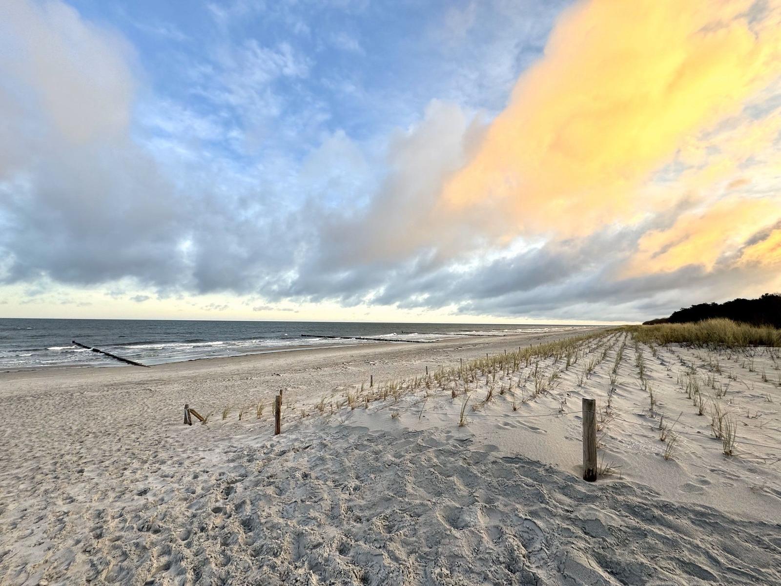 Strand mit Sanddünen und Blick aufs Meer bei Sonnenuntergang.