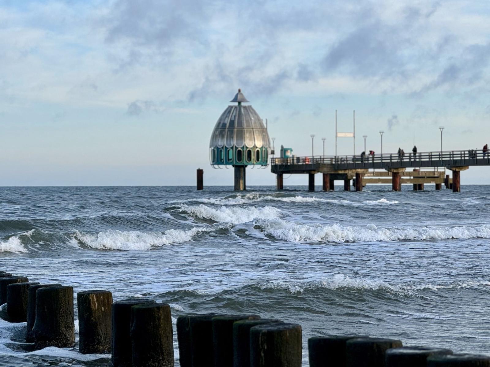 Küstenlandschaft mit Pier und markanter Kuppelstruktur im Hintergrund.