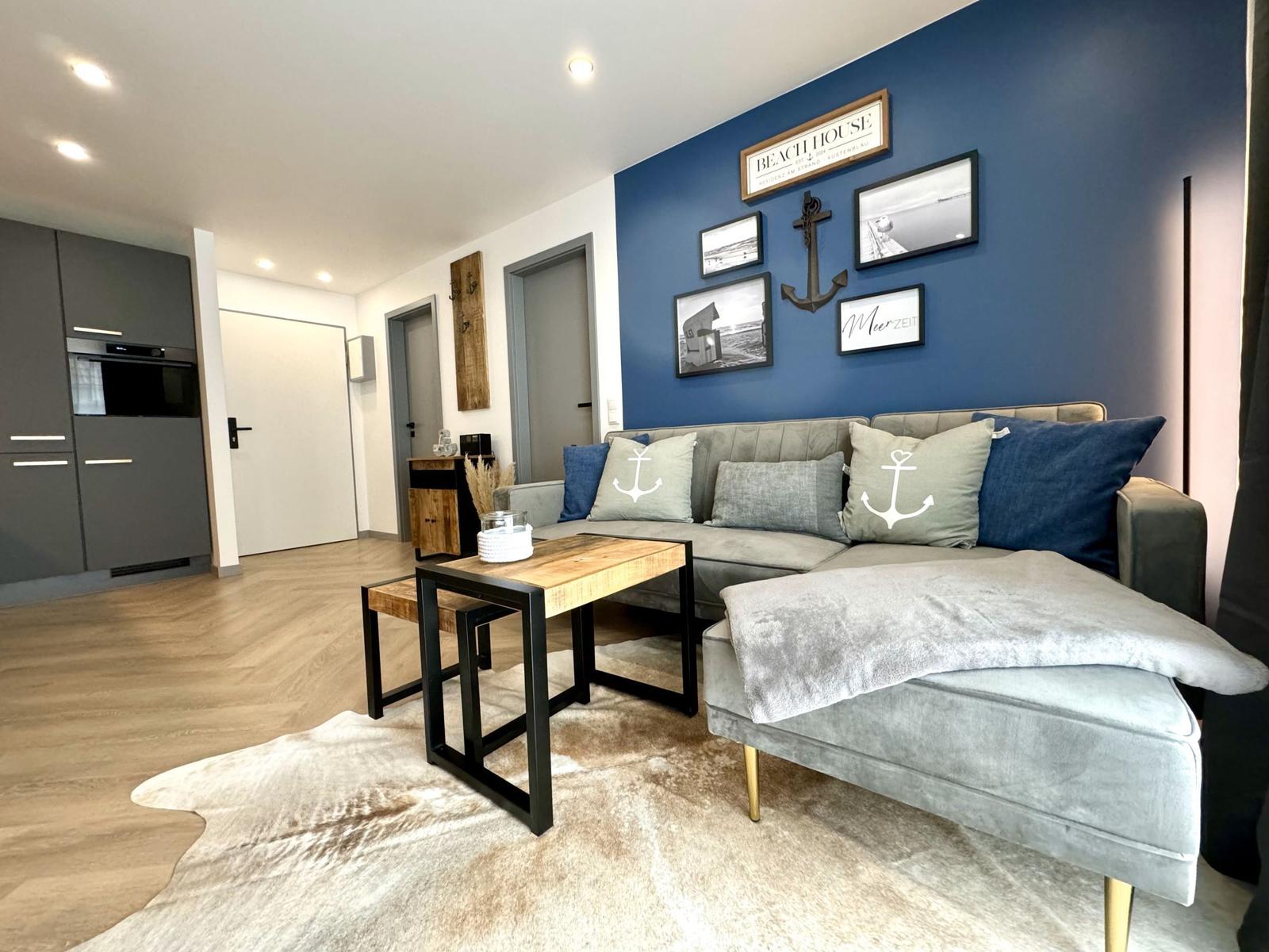 Wohnzimmer mit Sofa, Couchtisch und blauer Wand mit Dekoration.