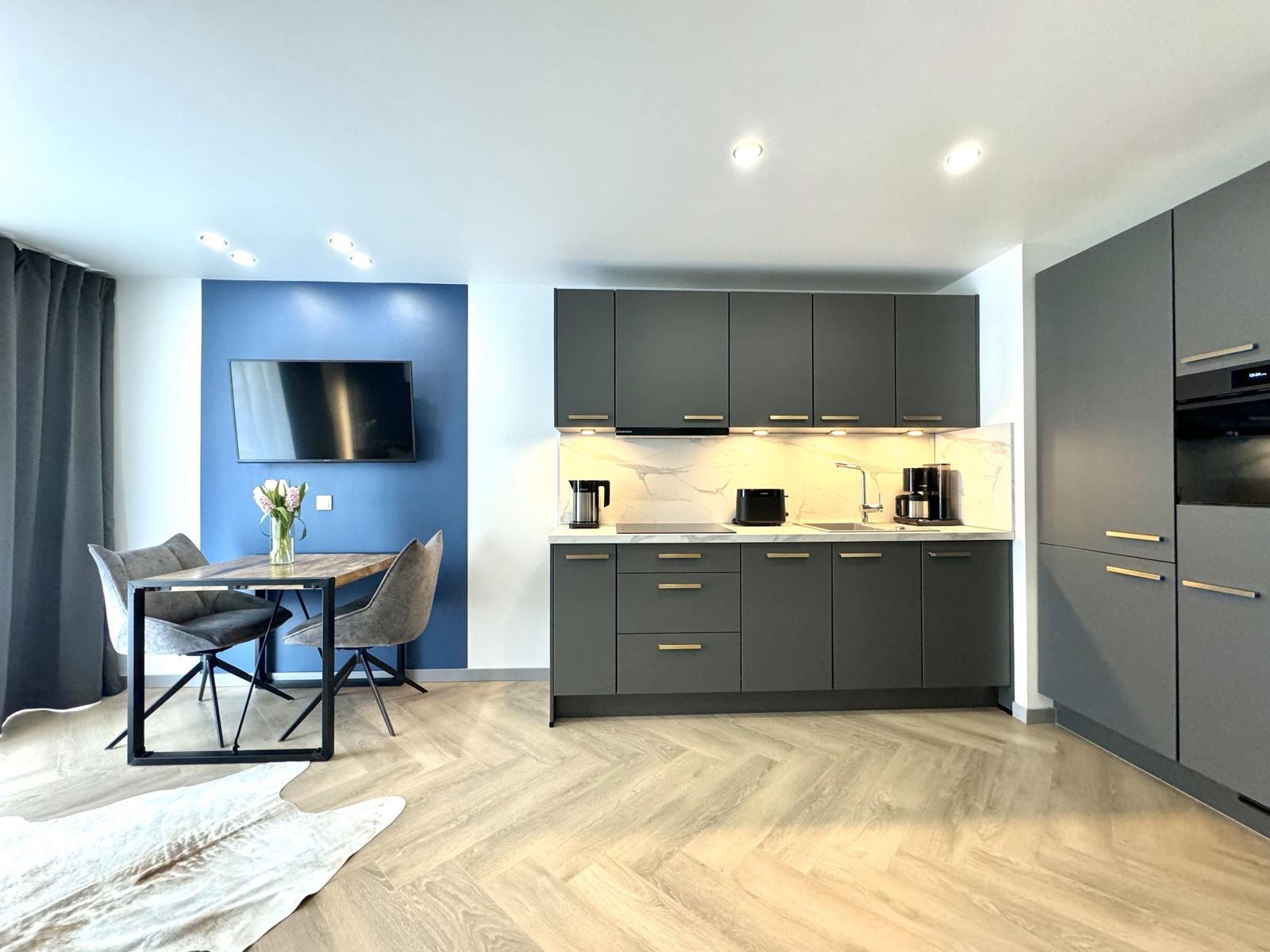 Moderne Küche mit Essbereich und Fernseher an blauer Wand.