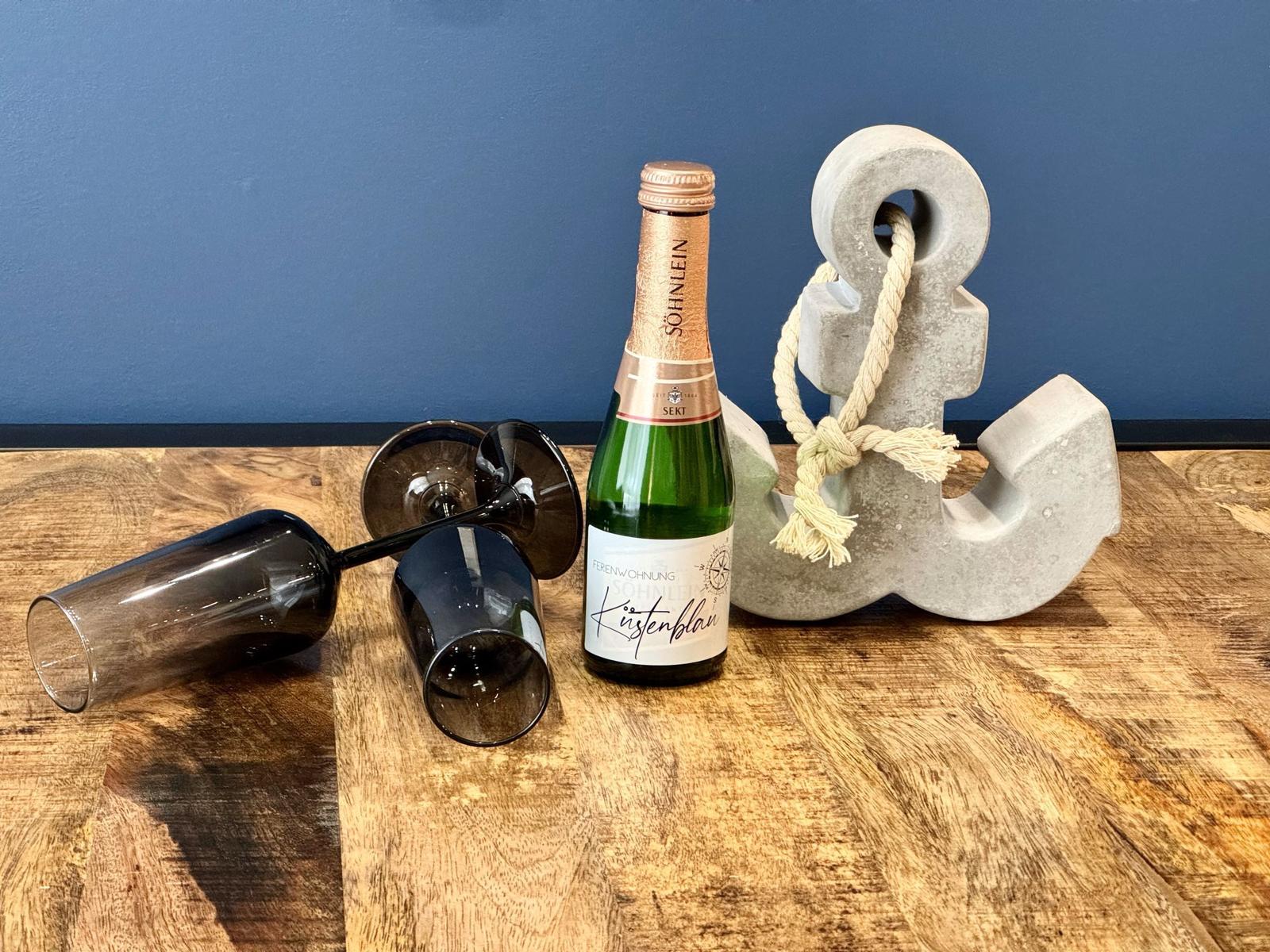 Eine Flasche Sekt, zwei Gläser und ein Anker auf einer Holzoberfläche.