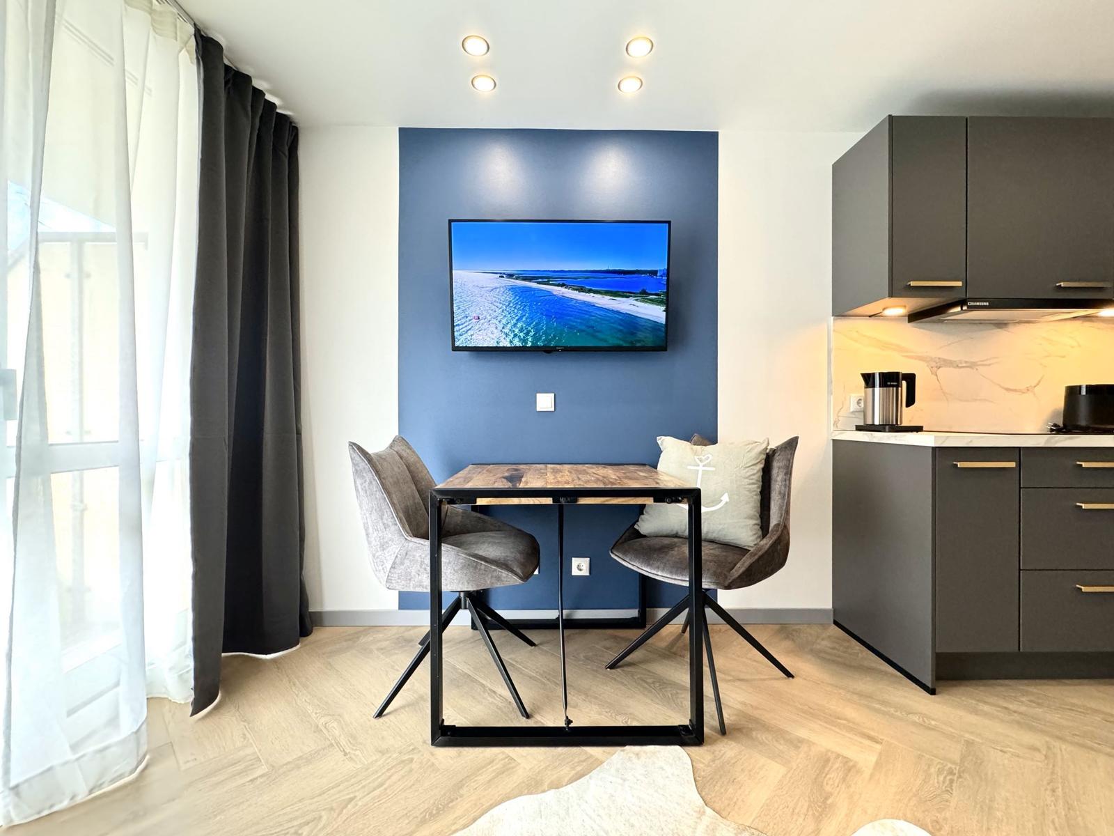 Küche mit Esstisch und Fernseher an blauer Wand.