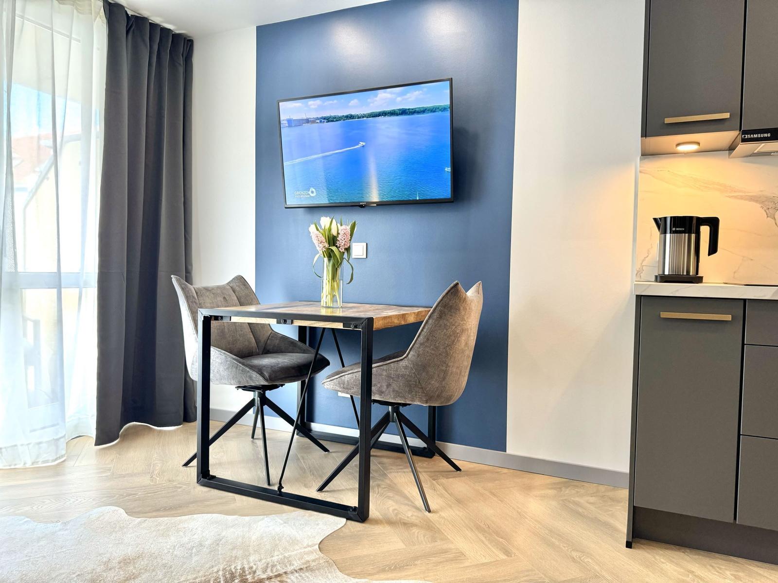 Essbereich mit Tisch, zwei Stühlen und Fernseher an blauer Wand.