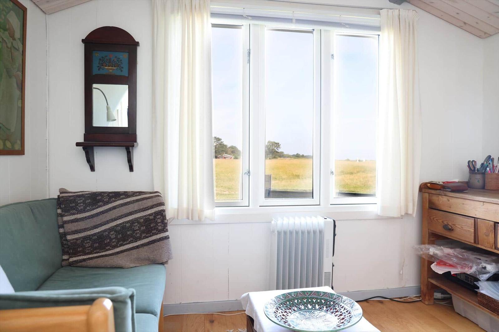 Ein Raum mit Sofa, Fenster und Holzmöbeln. Draußen ist ein Feld sichtbar.