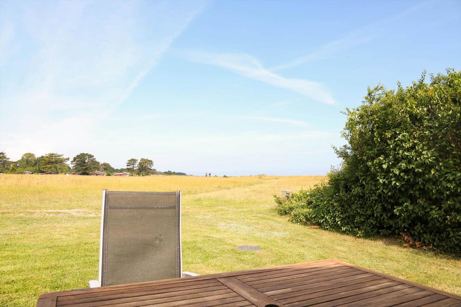 Terrasse mit Stuhl und Tisch, Blick auf grünes Feld und Himmel.