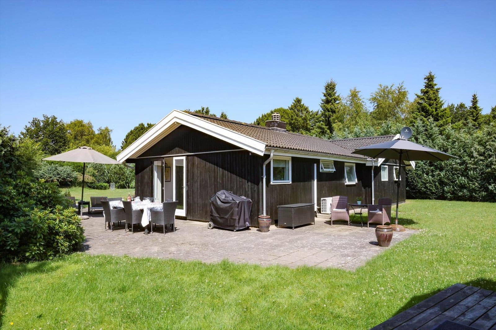 Ein Haus mit Terrasse, Garten und Außensitzgelegenheiten unter Sonnenschirmen.