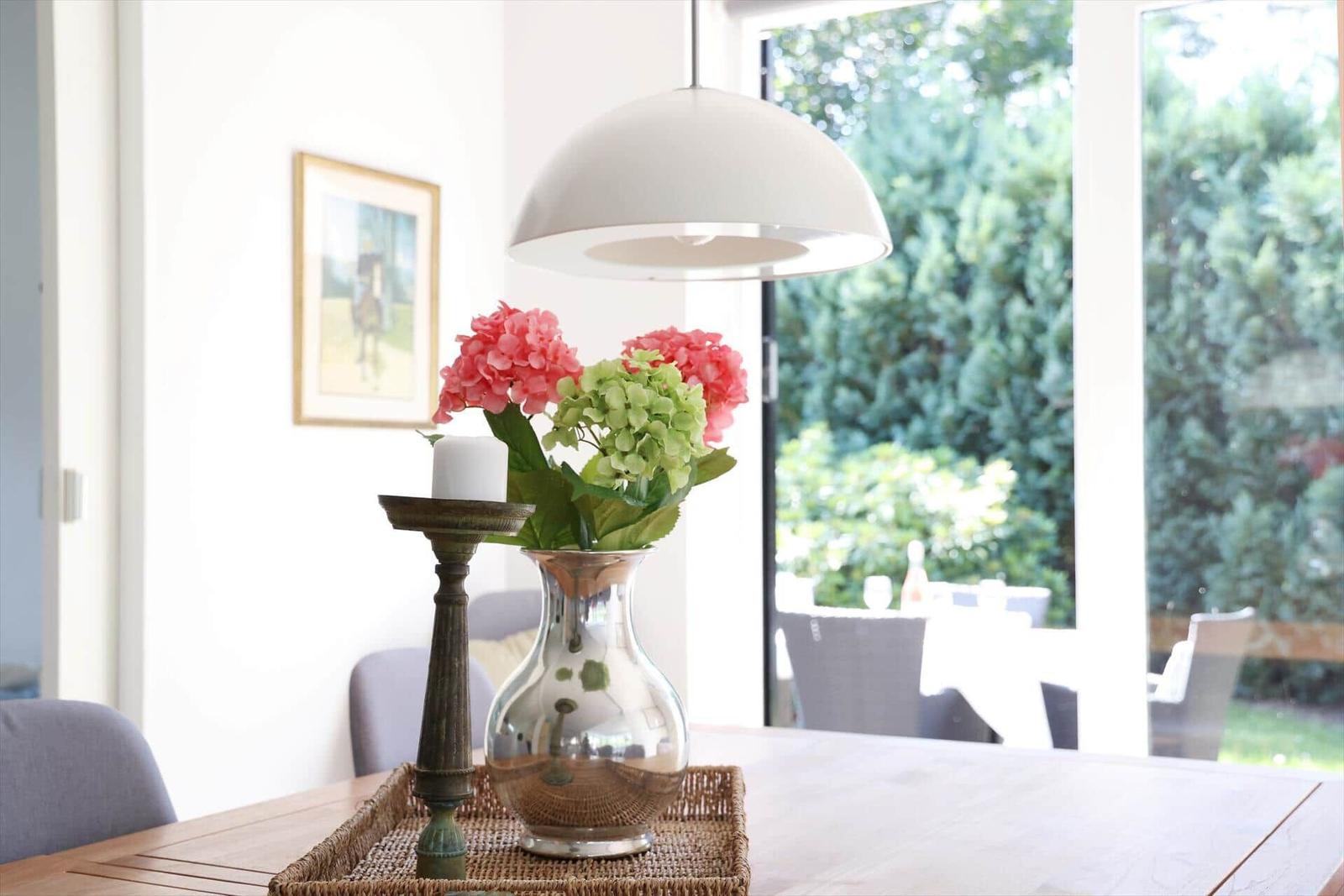 Esstisch mit Blumen und Laterne vor Fenster mit Gartenblick.