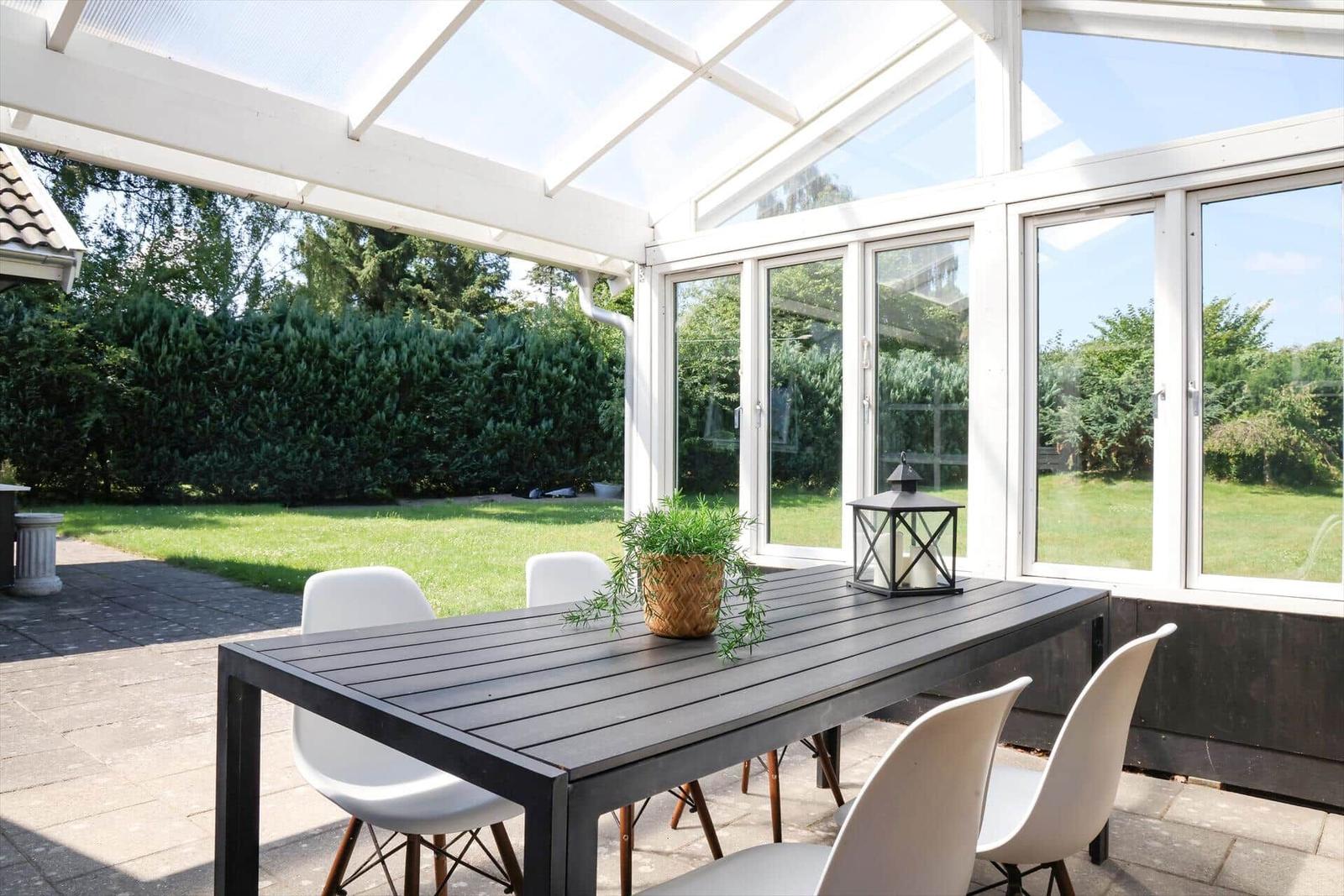 Terrasse mit Tisch und Stühlen unter Glasdach mit Blick auf Garten