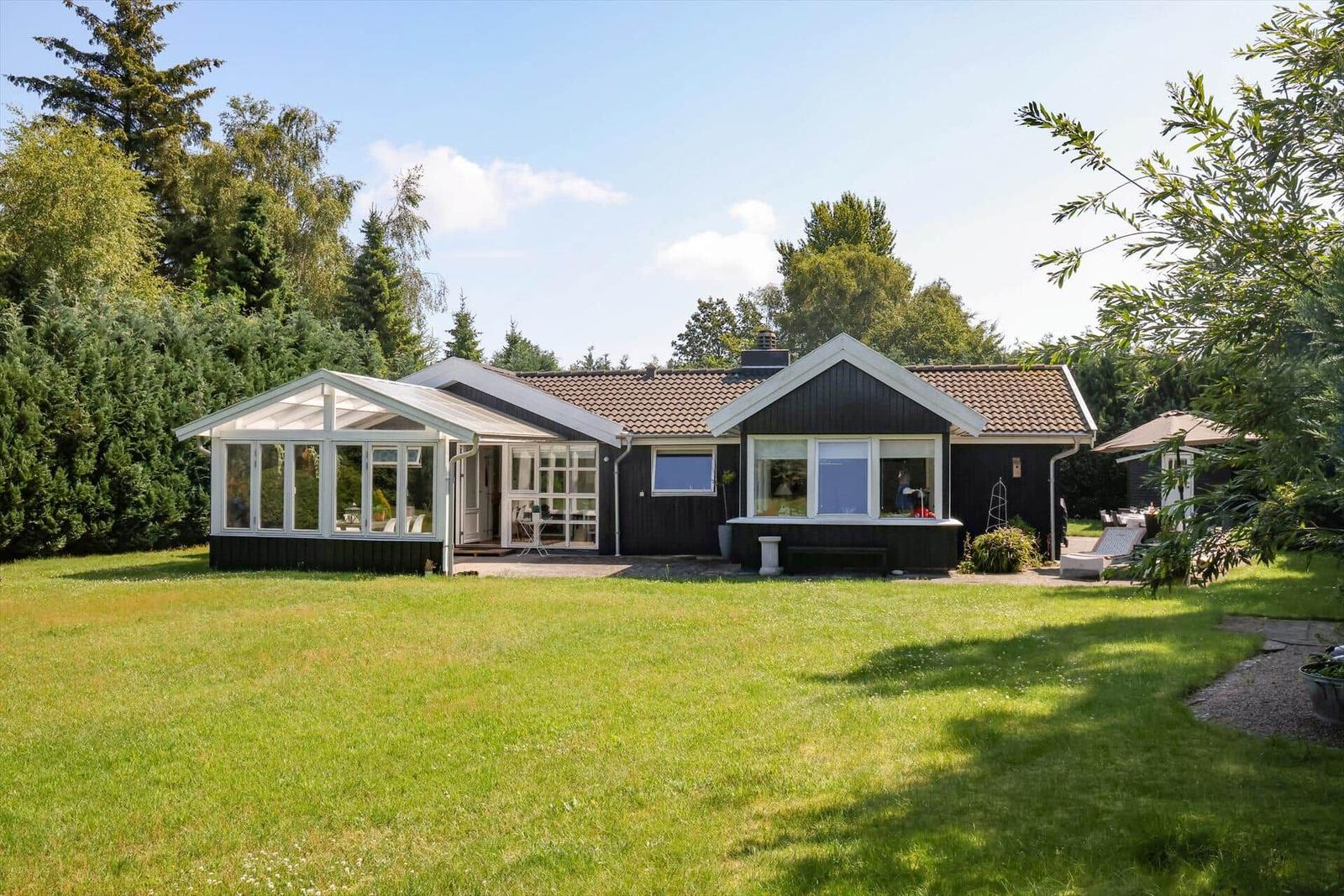 Ein Haus mit großem Garten und Terrasse. Weiße Fenster und dunkle Fassade.