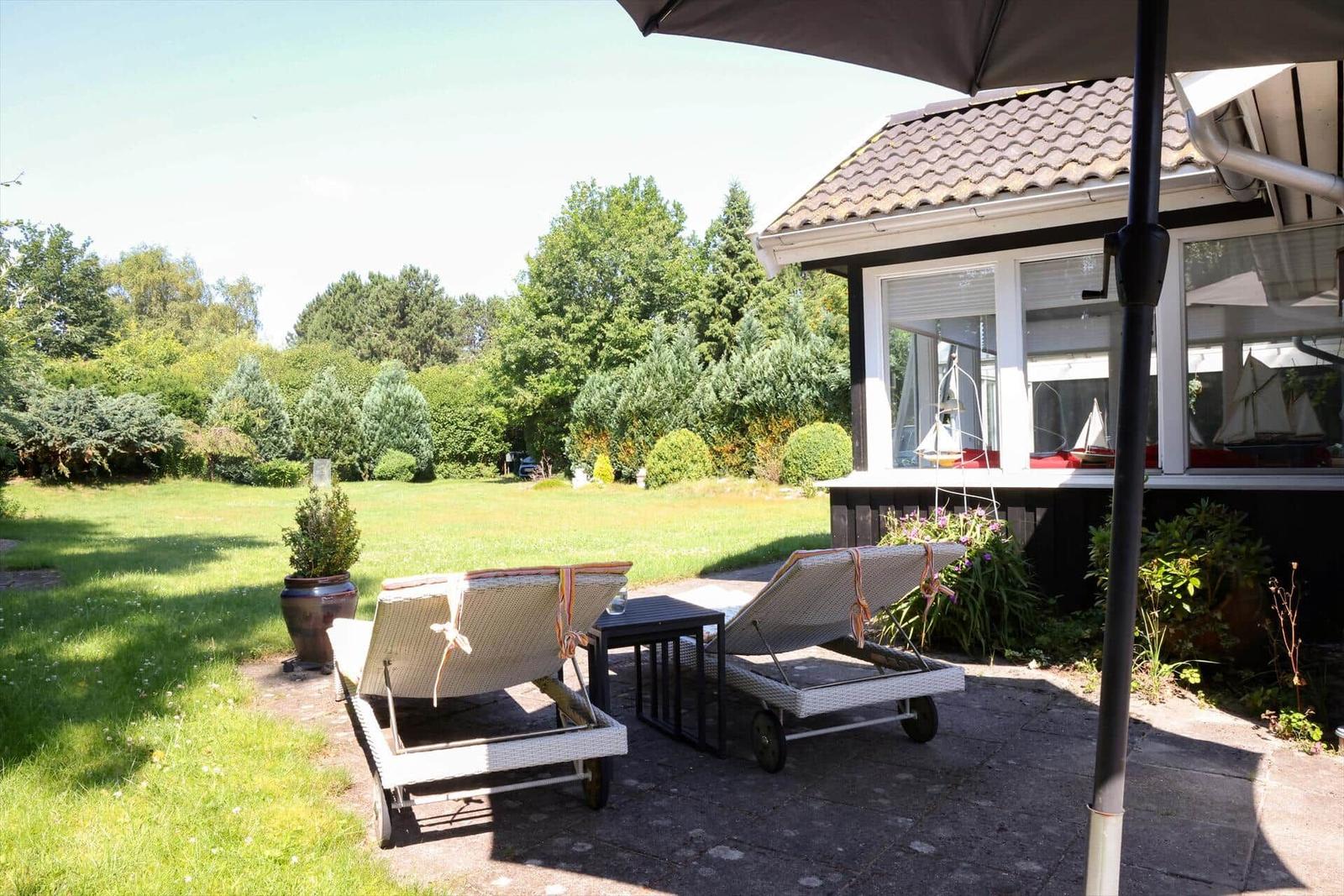Terrasse mit Liegestühlen und Sonnenschirm. Hinterhof mit Rasen und Bäumen.
