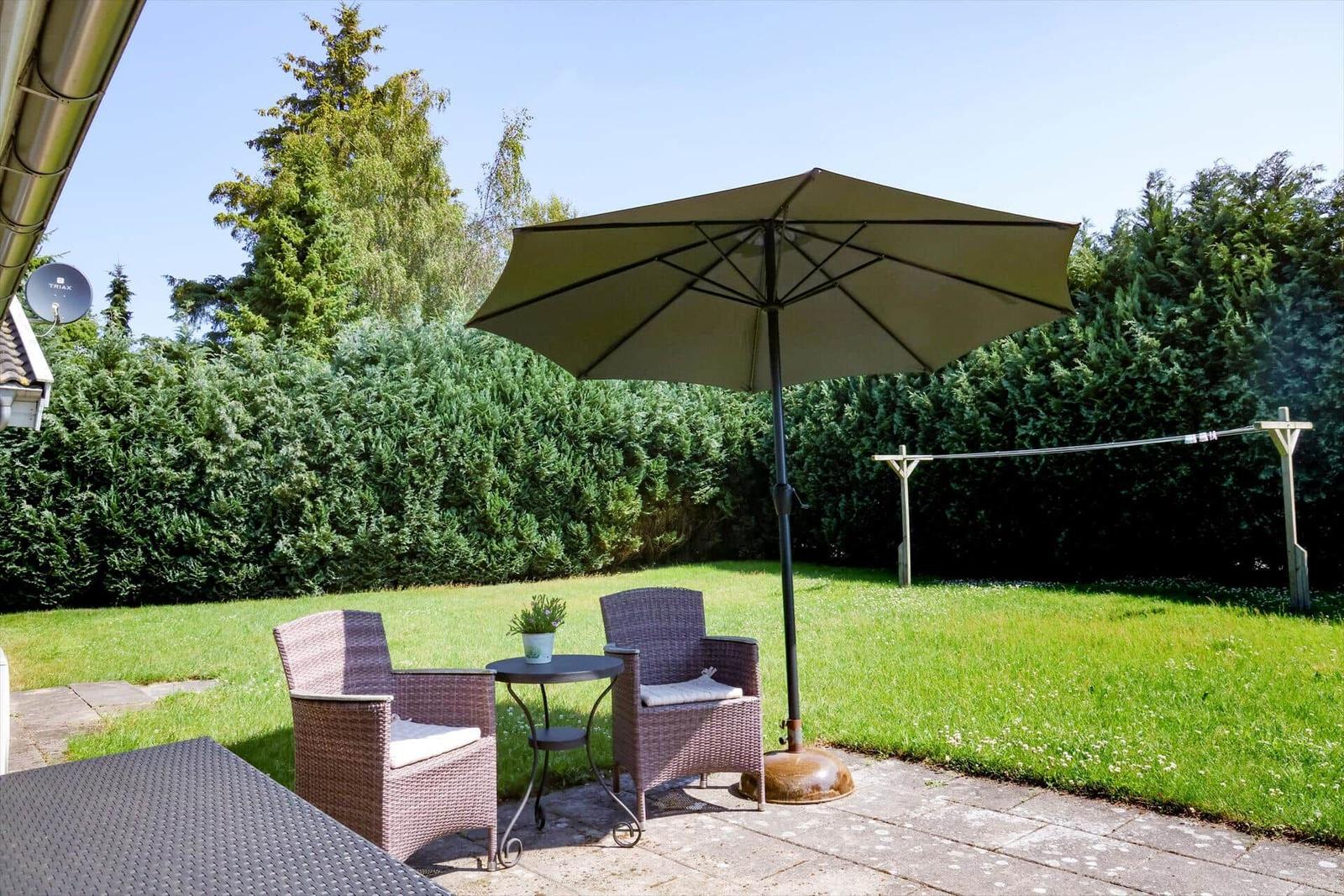 Terrasse mit Sitzgruppe, Sonnenschirm und Rasenfläche.