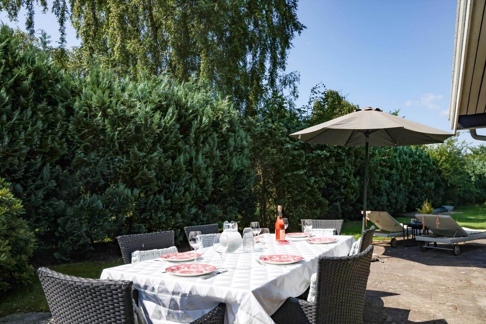 Garten mit gedecktem Tisch unter Sonnenschirm und Liegestühlen.