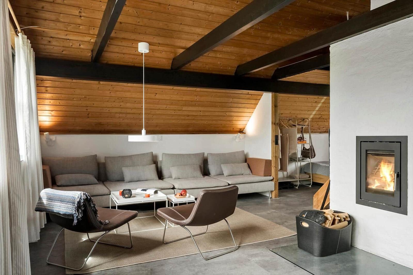 Wohnraum mit Sofa, Sesseln und Kamin. Holzdecke und Betonboden.