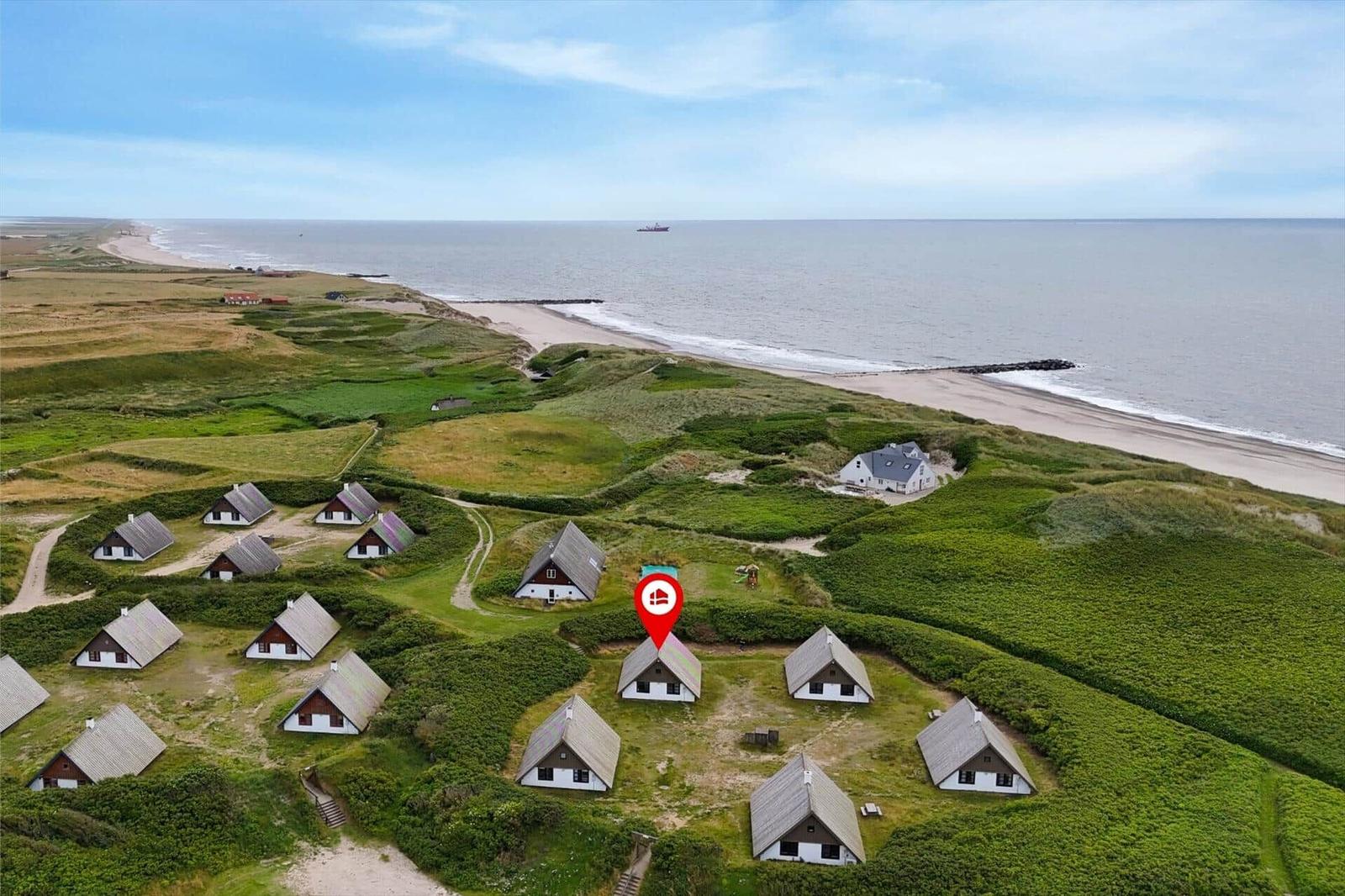Häuser am Strand mit grünen Dünen und Meer im Hintergrund.