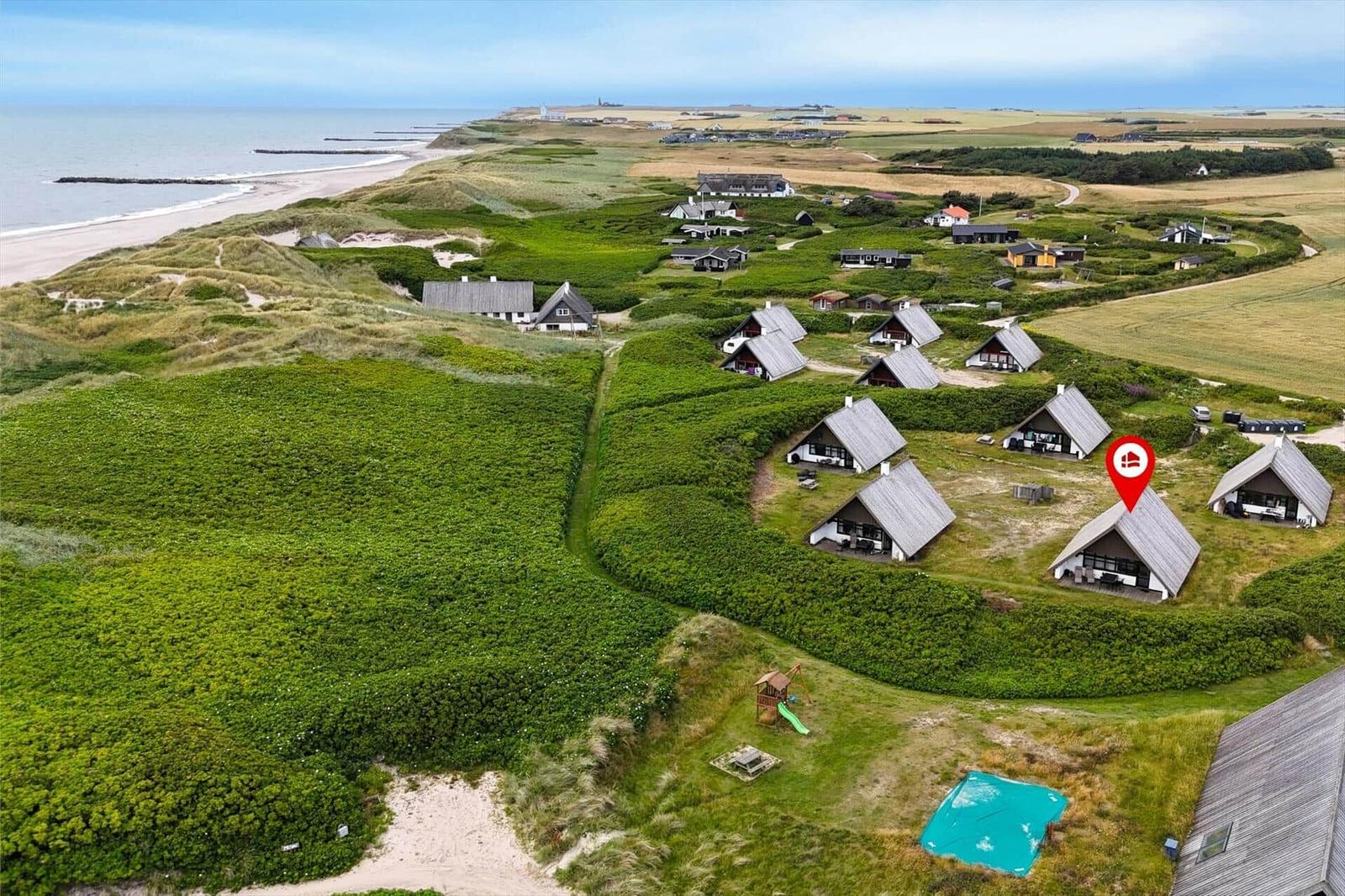 Aerial view of coastal cabins nestled among green dunes and fields near the sea.