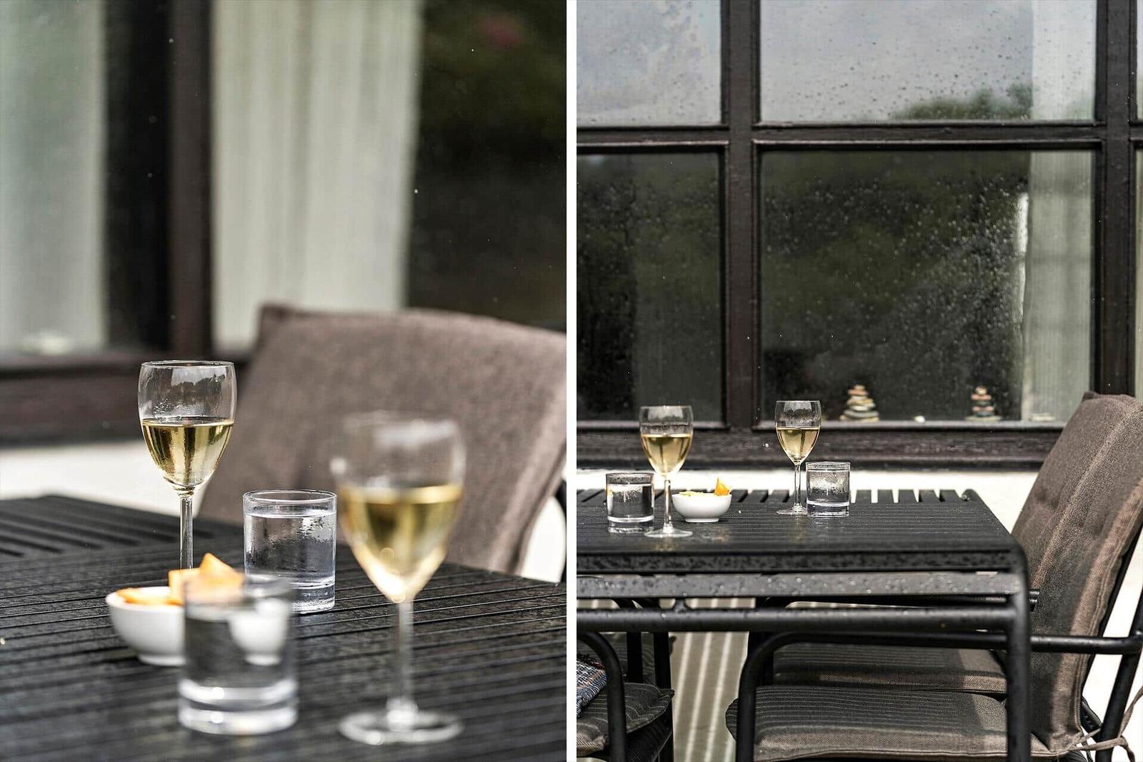 Tisch mit Gläsern und kleinen Schalen auf Terrasse vor Fenster mit Regentropfen.