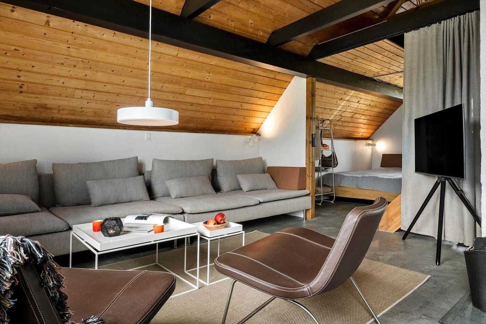 Wohnbereich mit Sofa, Sessel und Fernseher unter Holzdecke.