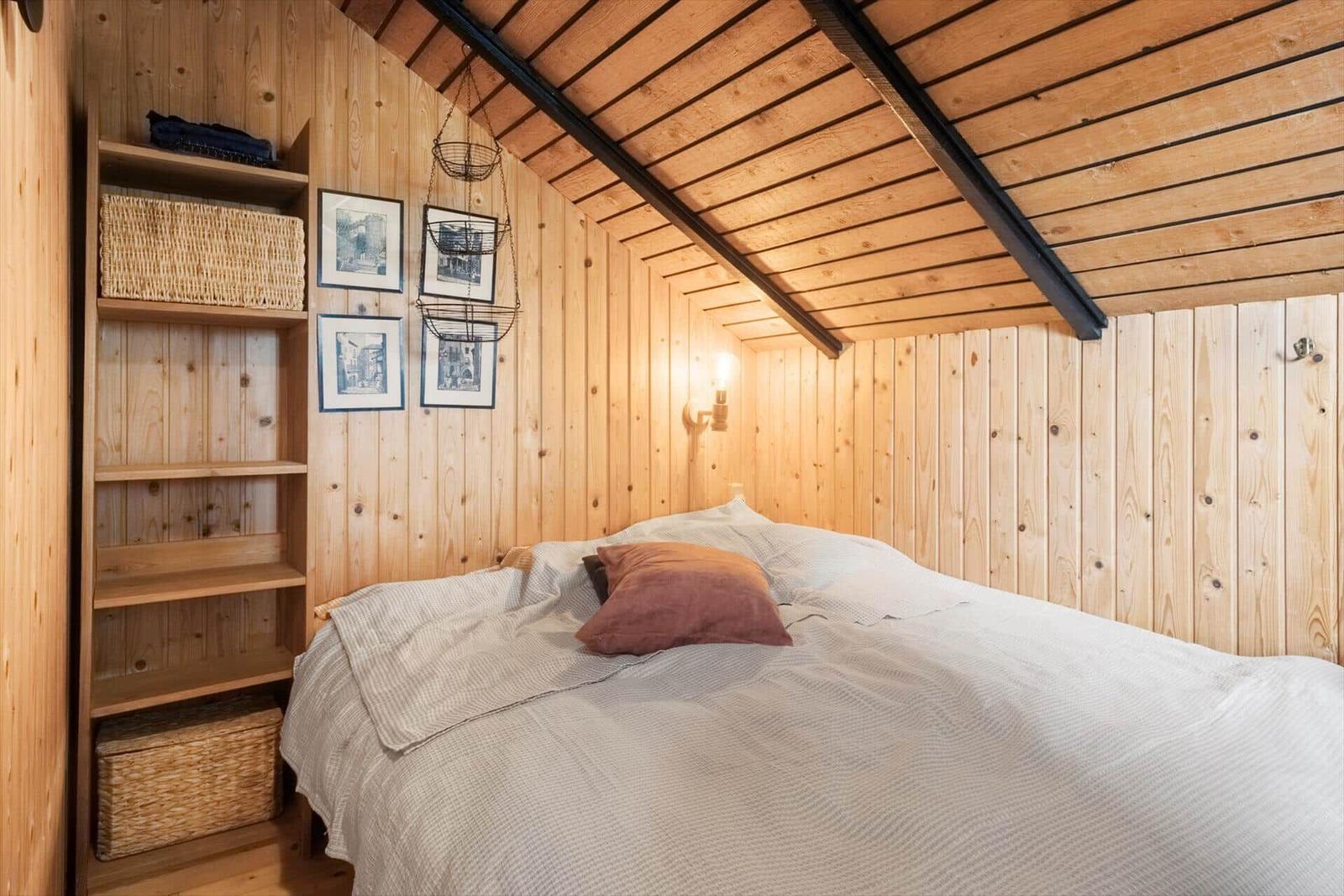 Schlafzimmer mit Holzwand, Bett und Regal. Decke mit Holz und schwarzen Balken.
