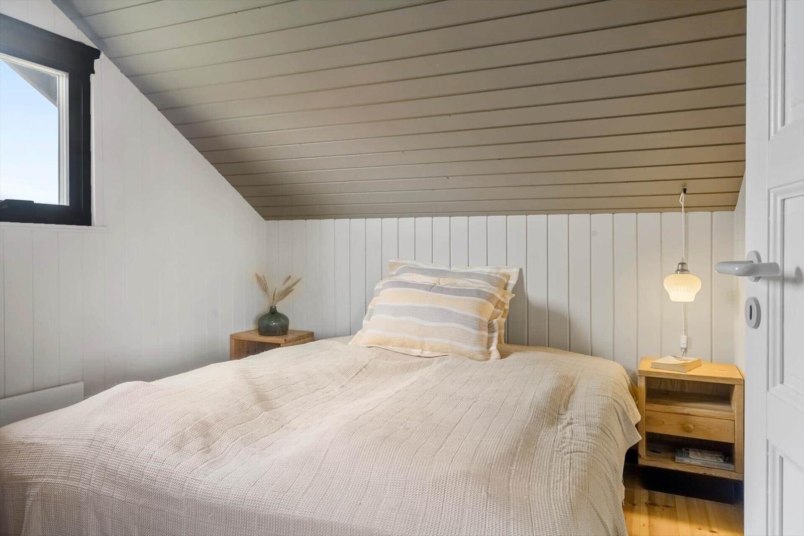 Schlafzimmer mit Dachschräge, Bett, Nachttisch und Lampe.