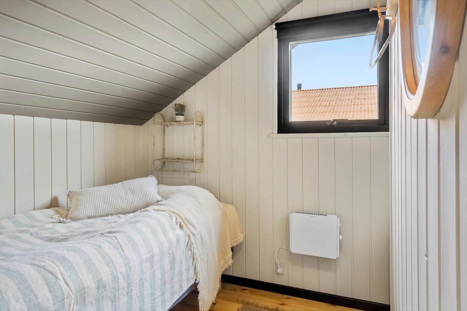 Schlafzimmer mit Bett, Wandregal und Fenster mit Blick auf Dach