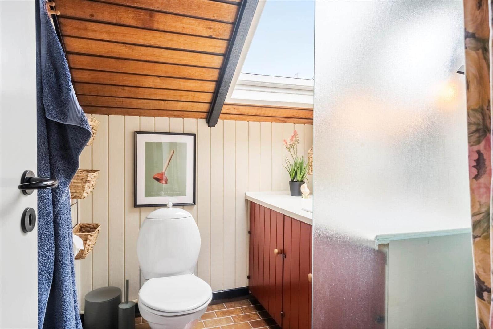 Badezimmer mit Toilette, Waschbecken und Dusche unter Holzdecke.