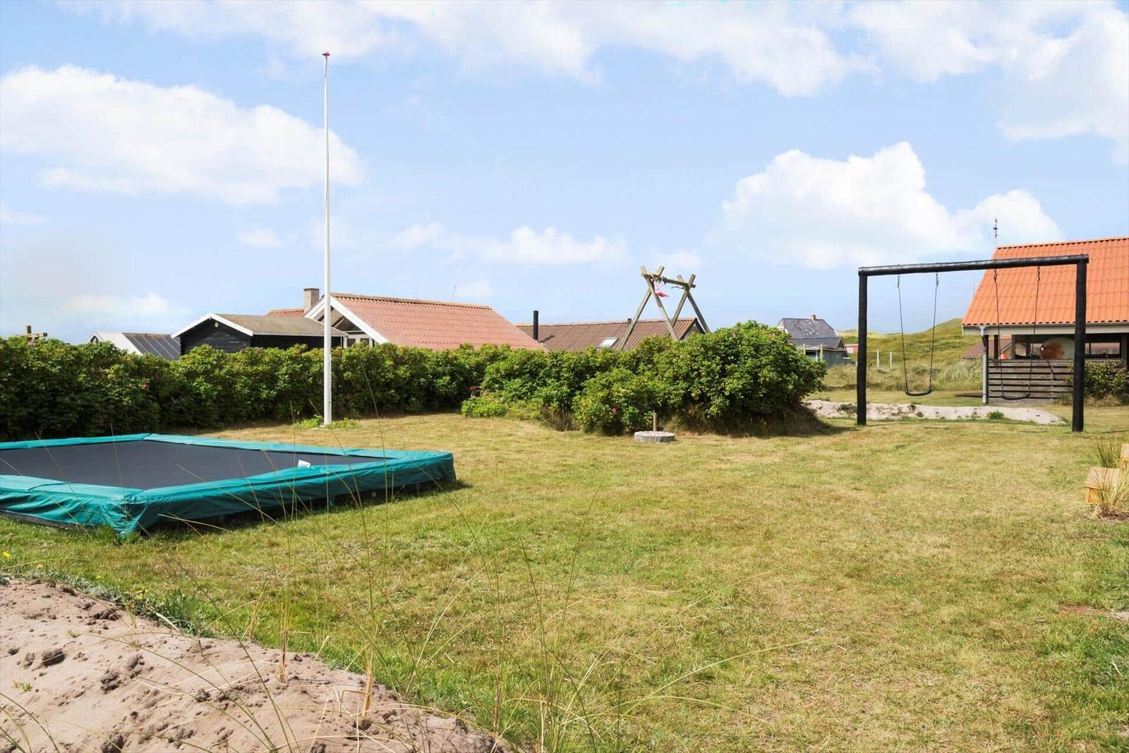 Grüner Garten mit Trampolin, Schaukel und Heckenzaun. Hintergrund: Häuser mit Dächern.