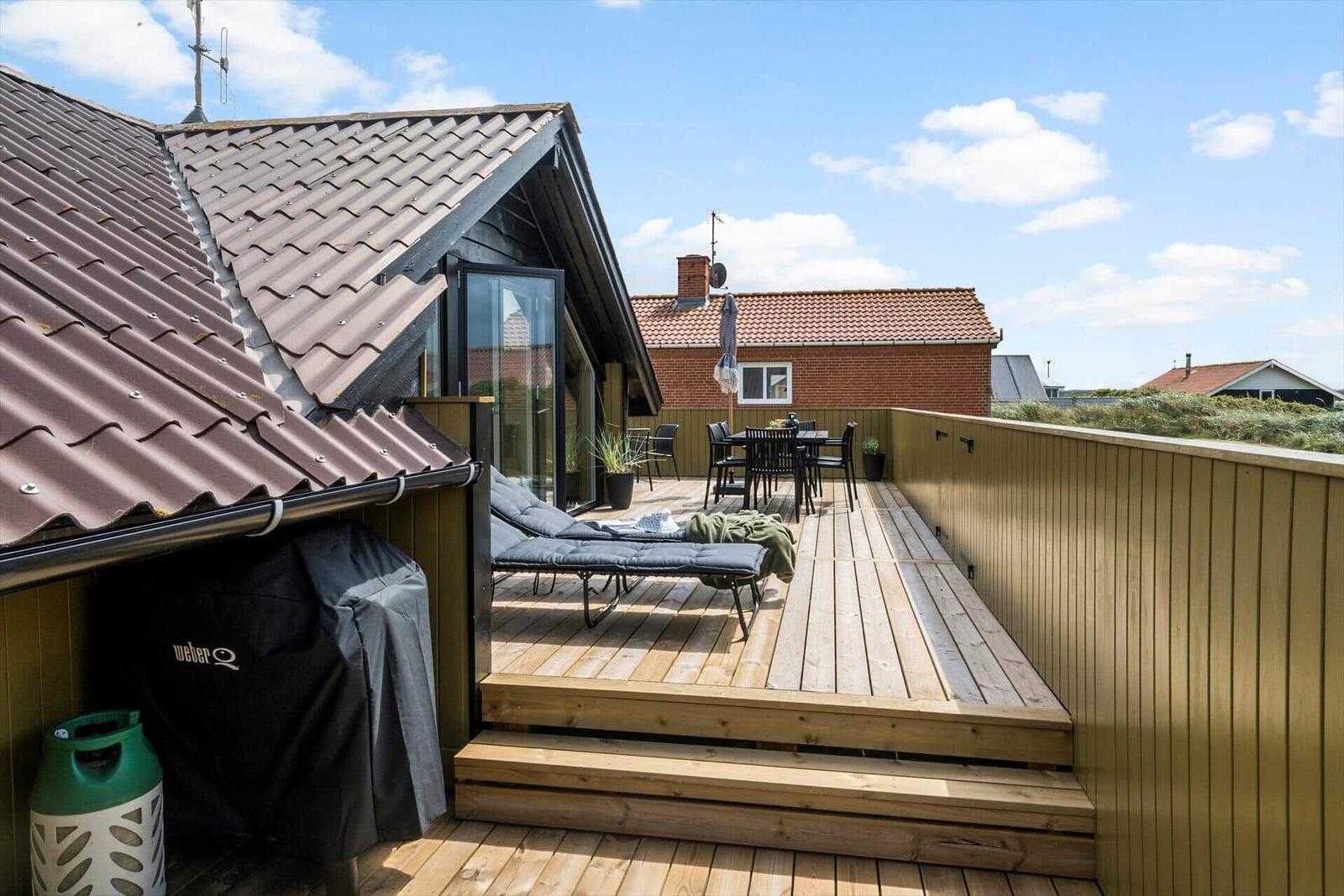 Terrasse mit Liegen, Tisch und Stühlen, Blick auf Wohnhaus und Strand.