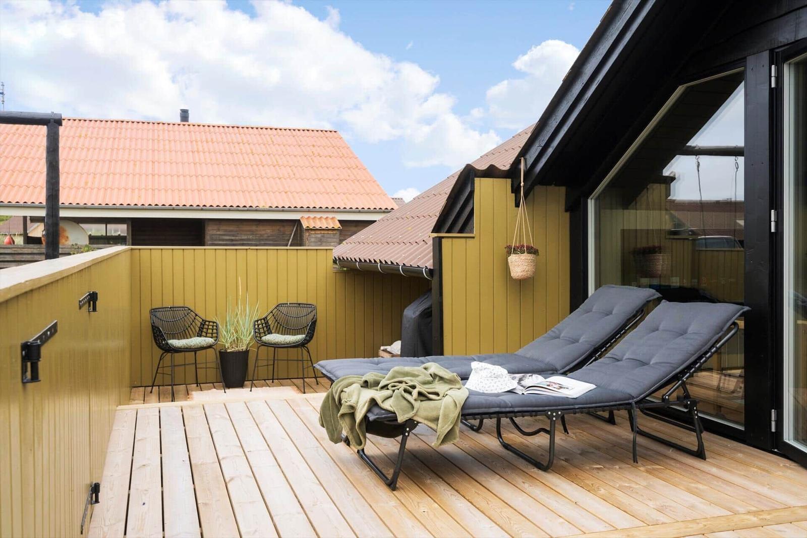 Terrasse mit Liegestühlen, Sitzgelegenheit und Pflanzen an gelbem Holzgeländer.