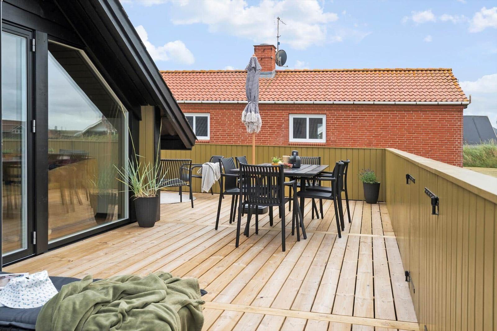 Terrasse mit Tisch, Stühlen und Sonnenschirm. Holzdecke und Blick auf roten Backsteinbau.