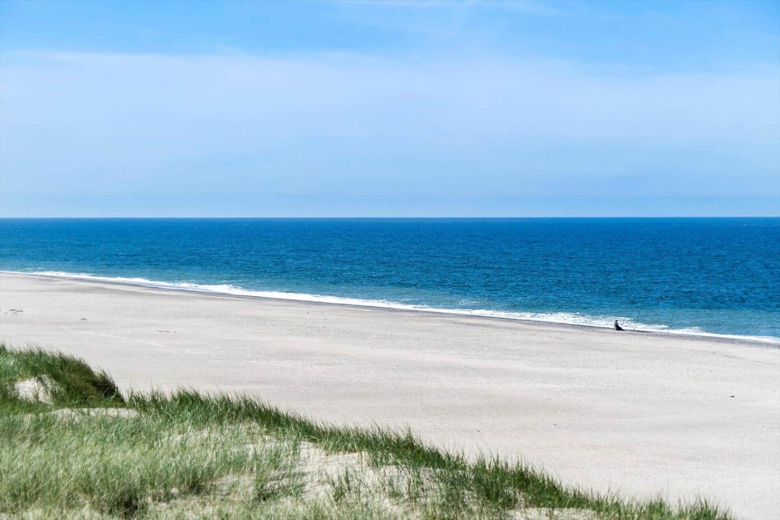 Weiterer Blick auf den Strand und das Meer mit Dünen im Vordergrund.