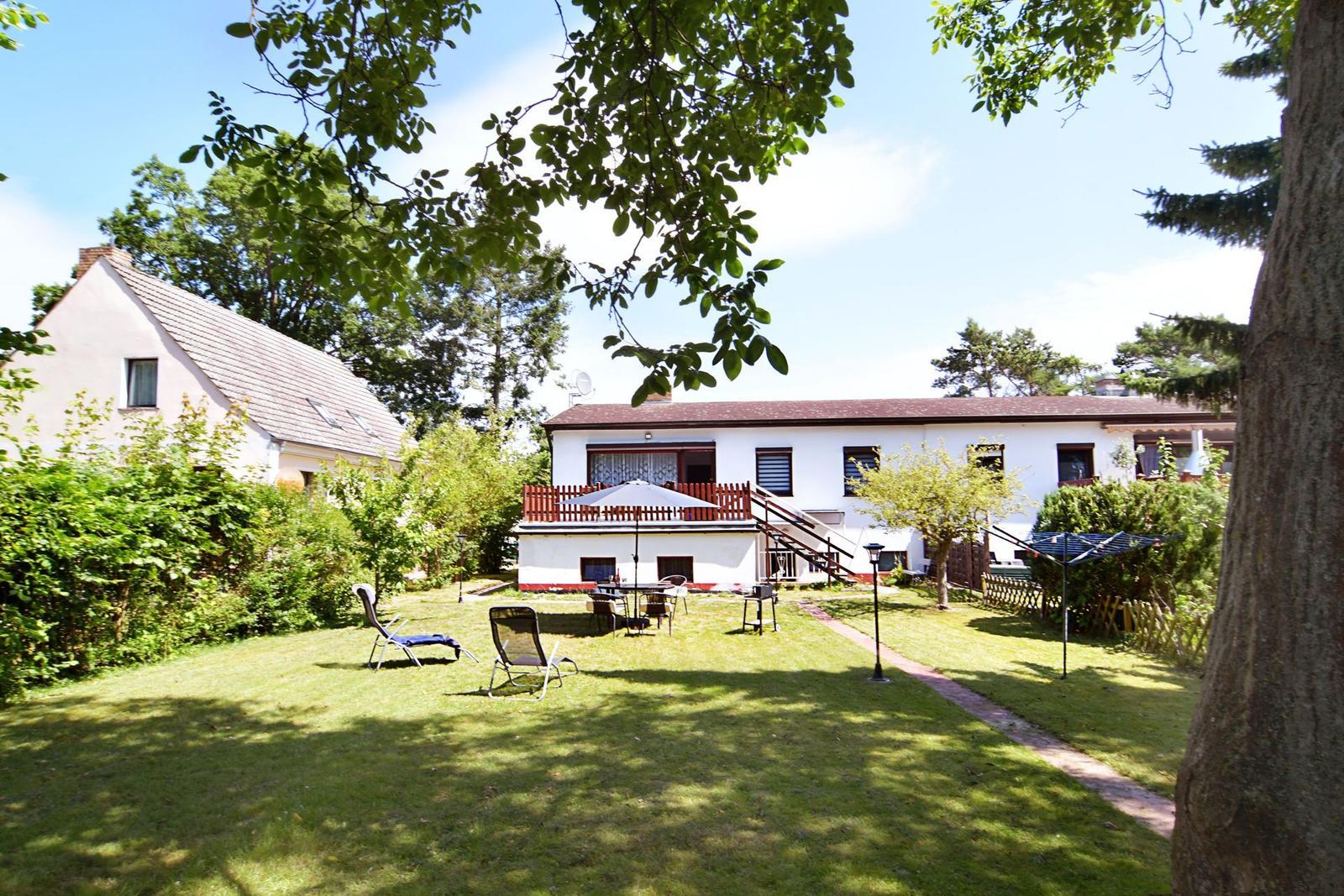 Haus mit Garten, Terrasse und Liegestühlen unter Bäumen.