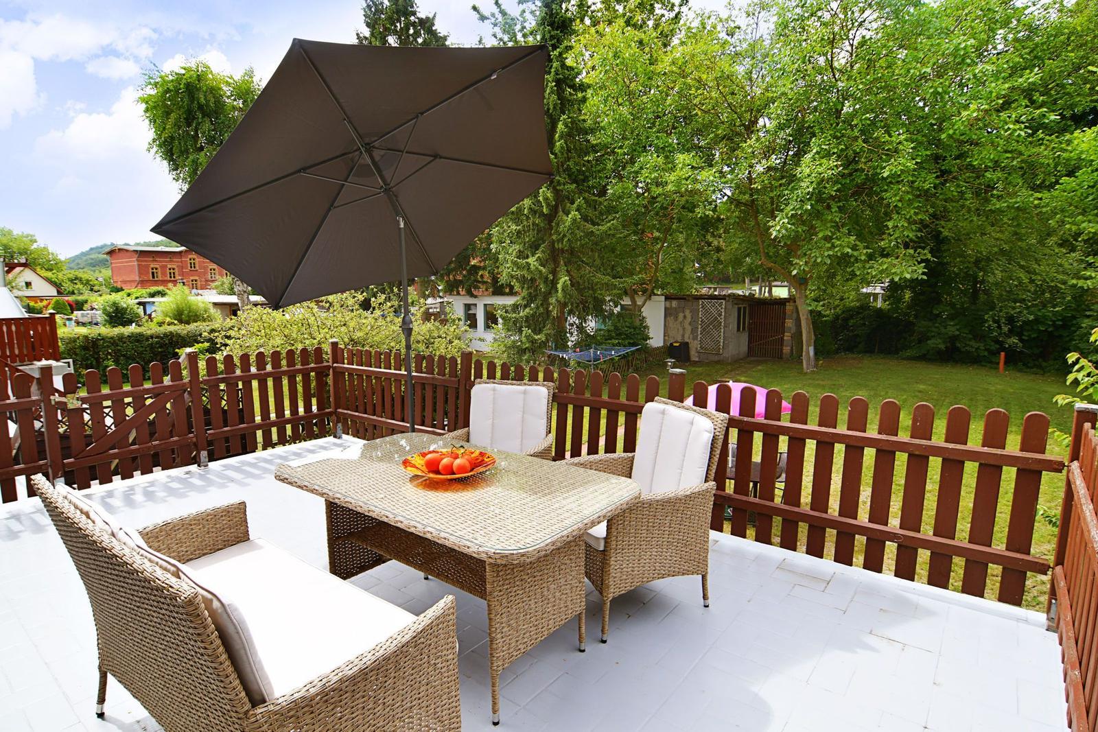 Terrasse mit Tisch, Stühlen und Sonnenschirm. Hinterhof mit Grünfläche und Zaun.