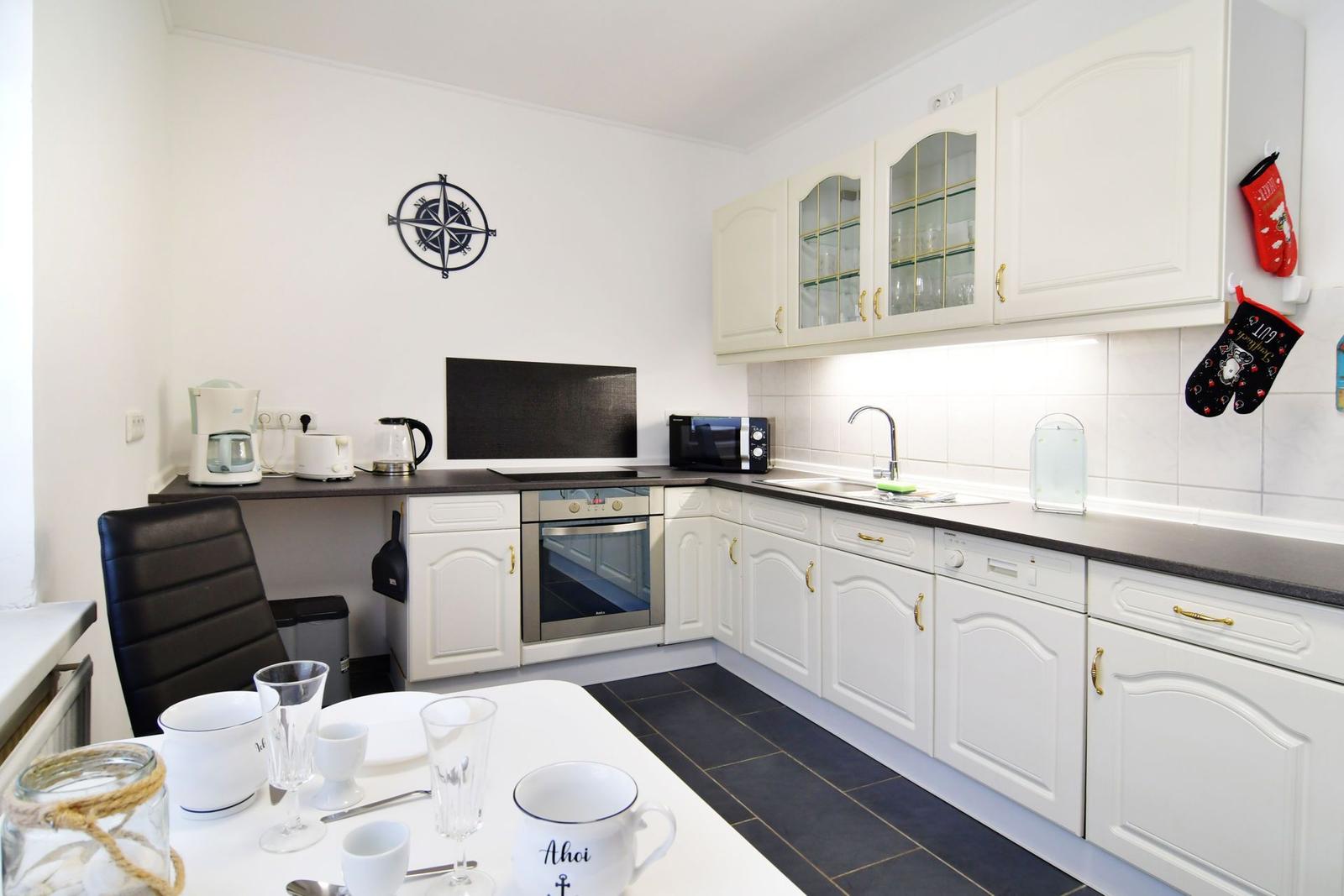 Küche mit weißen Schränken, dunkler Arbeitsplatte und Küchentisch mit Geschirr.