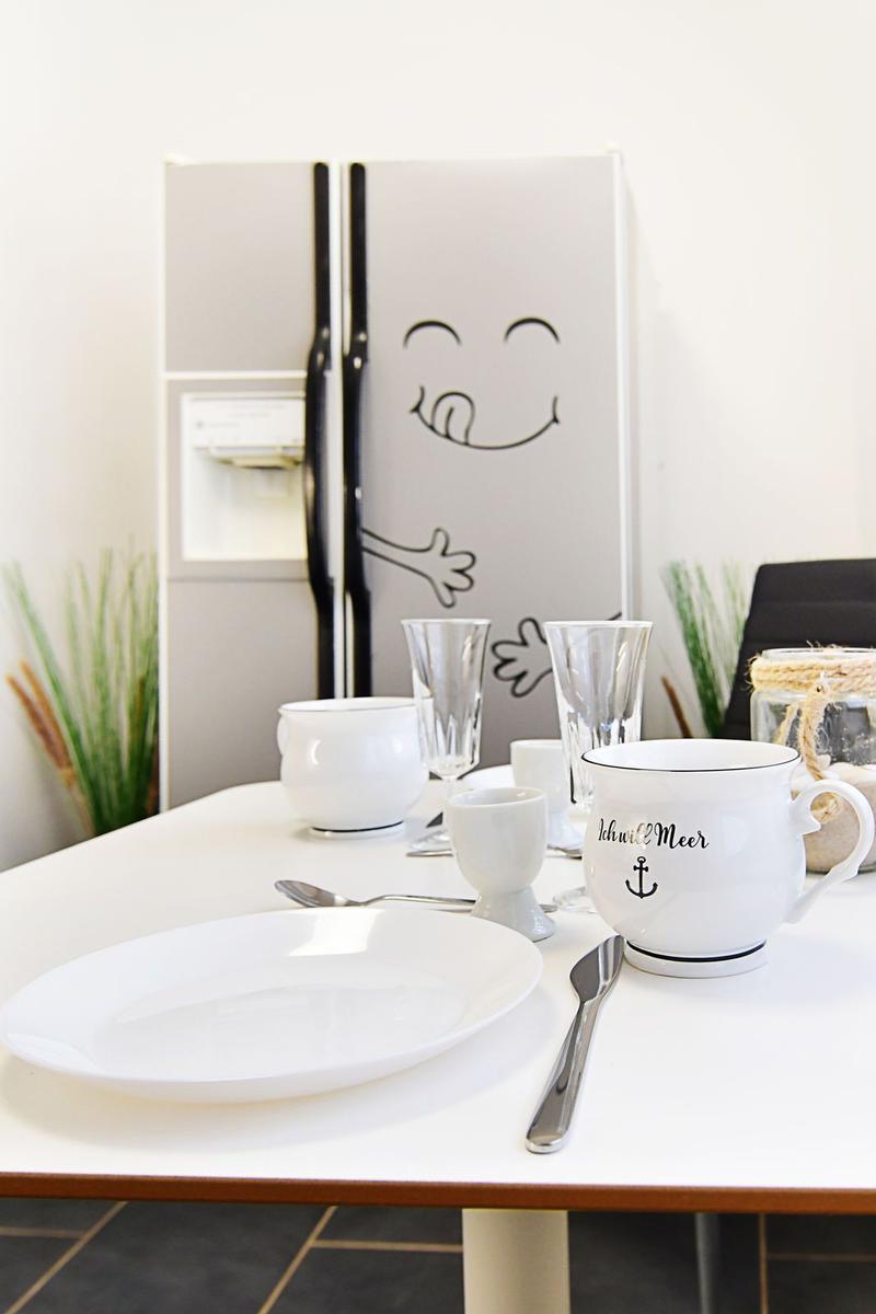 Küchenbereich mit Tisch, Geschirr und Kühlschrank mit Zeichnung.