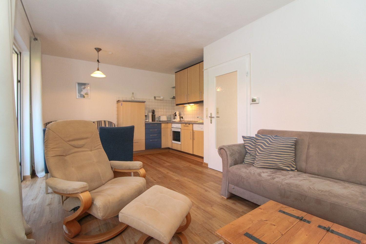 Wohnzimmer mit Sofa, Sessel und Küchenbereich.