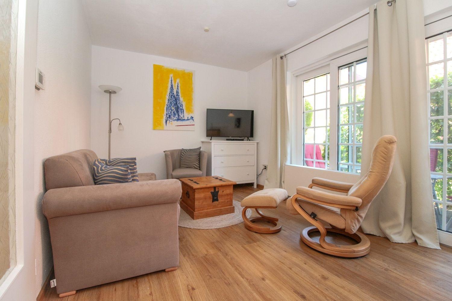 Wohnzimmer mit Sofa, Sessel, Fernseher und Holzboden.