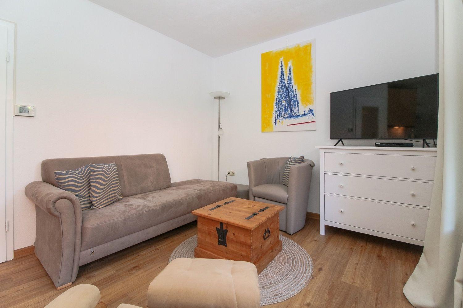 Wohnzimmer mit Sofa, Sessel, Fernseher und Holzkiste.