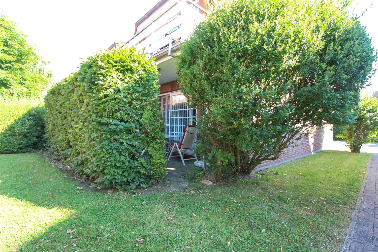 Hinterhof mit Garten, Beete und Sitzgelegenheit unter Bäumen.