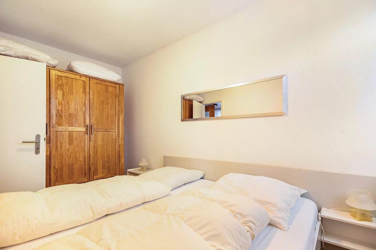 Schlafzimmer mit Doppelbett, Holzschrank und Spiegel an der Wand.
