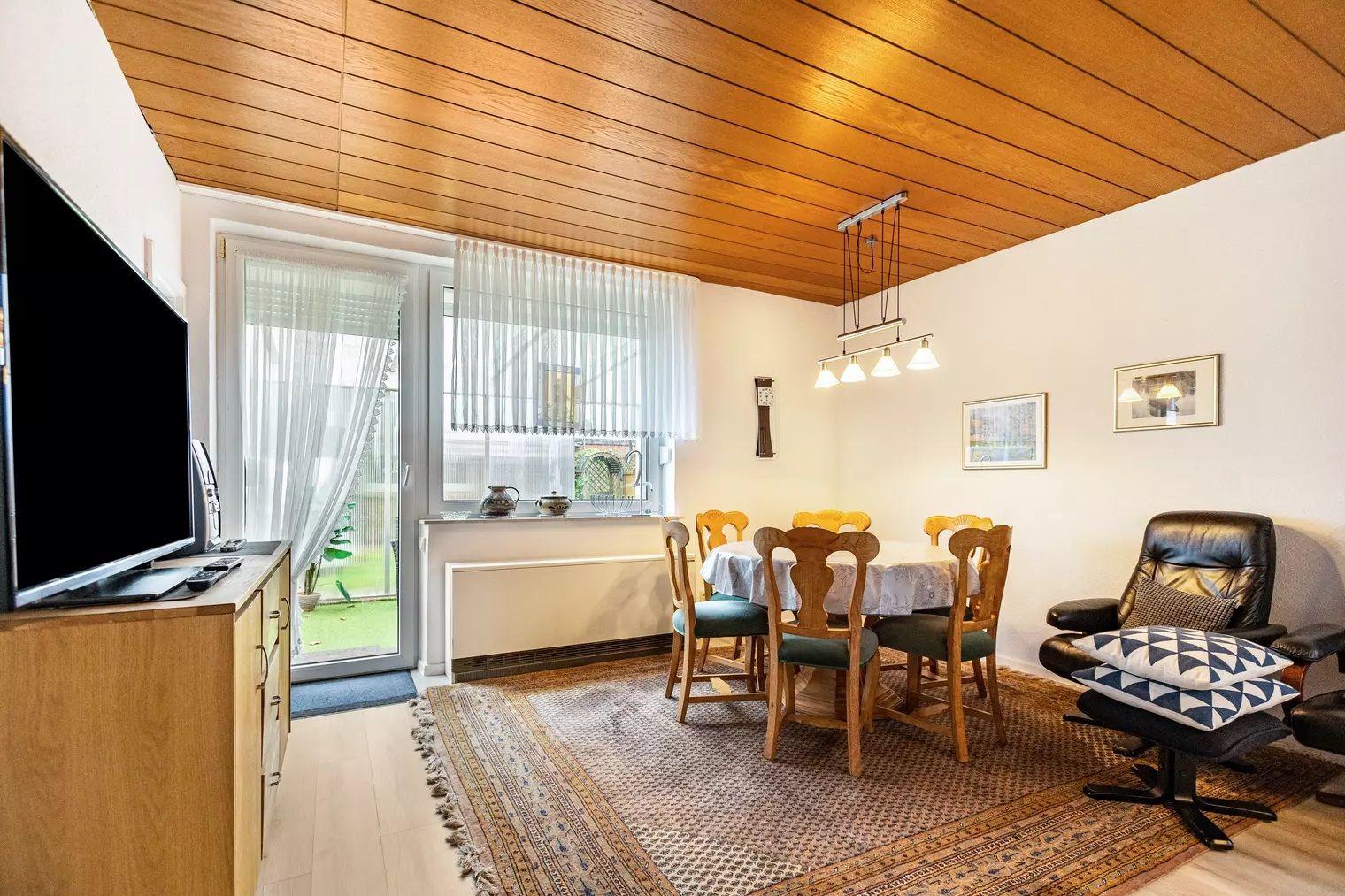 Esszimmer mit Holzdecke, Tisch mit Stühlen und Fernseher an der Wand.