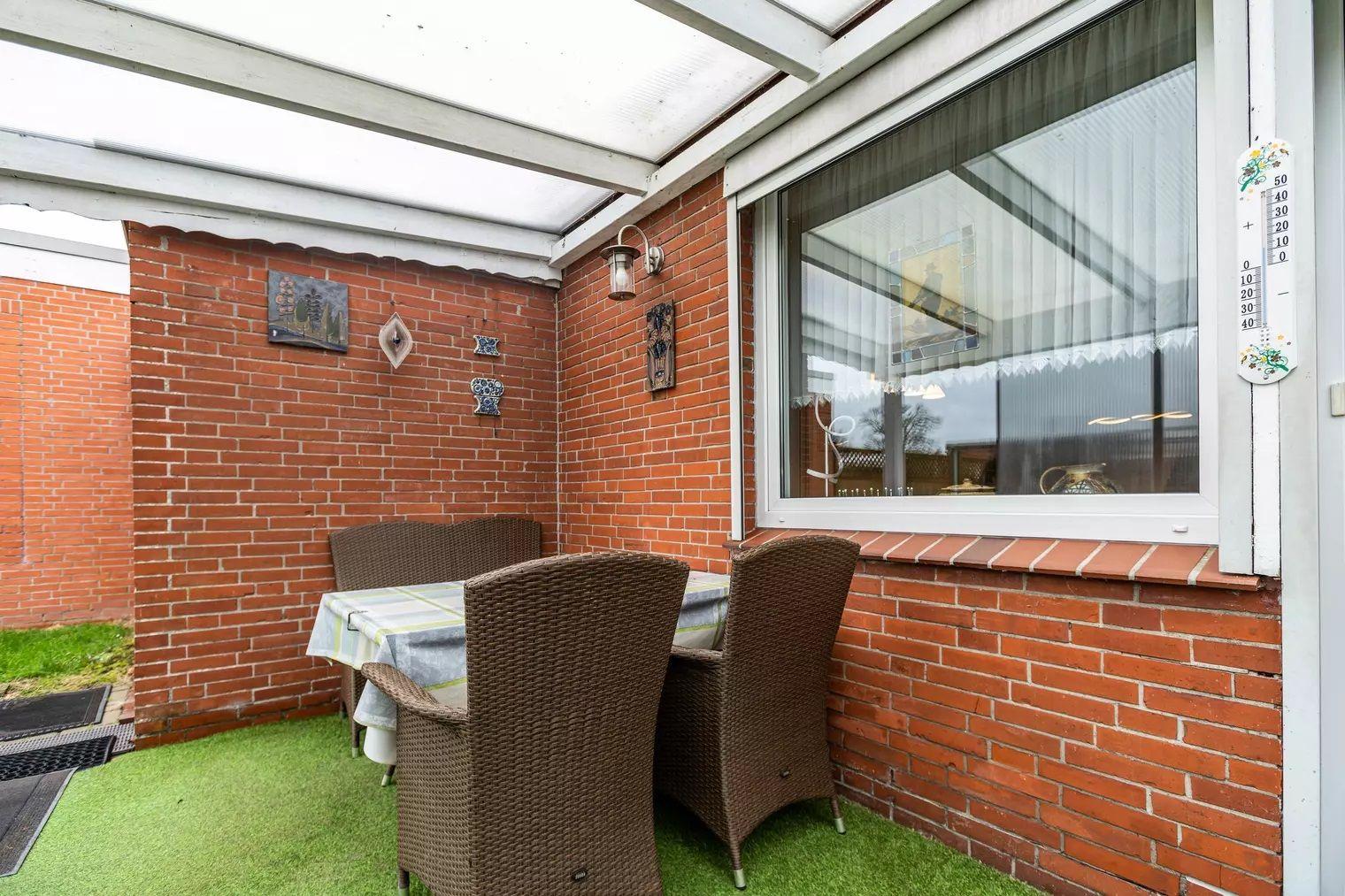 Terrasse mit Tisch, Stühlen und grünem Boden, an roten Ziegelwänden angebracht.