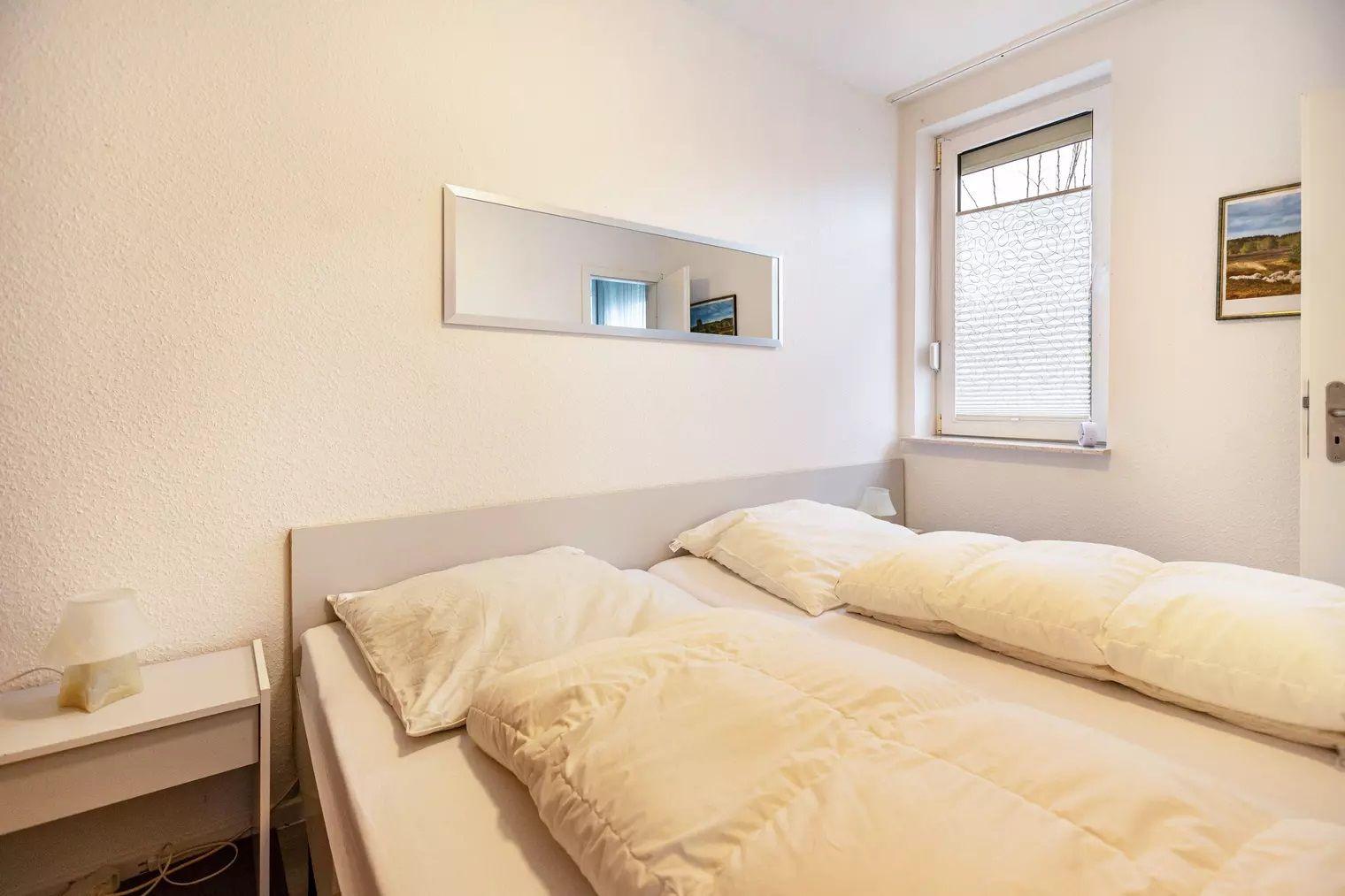 Schlafzimmer mit Doppelbett, Spiegel und Fenster mit Jalousie.