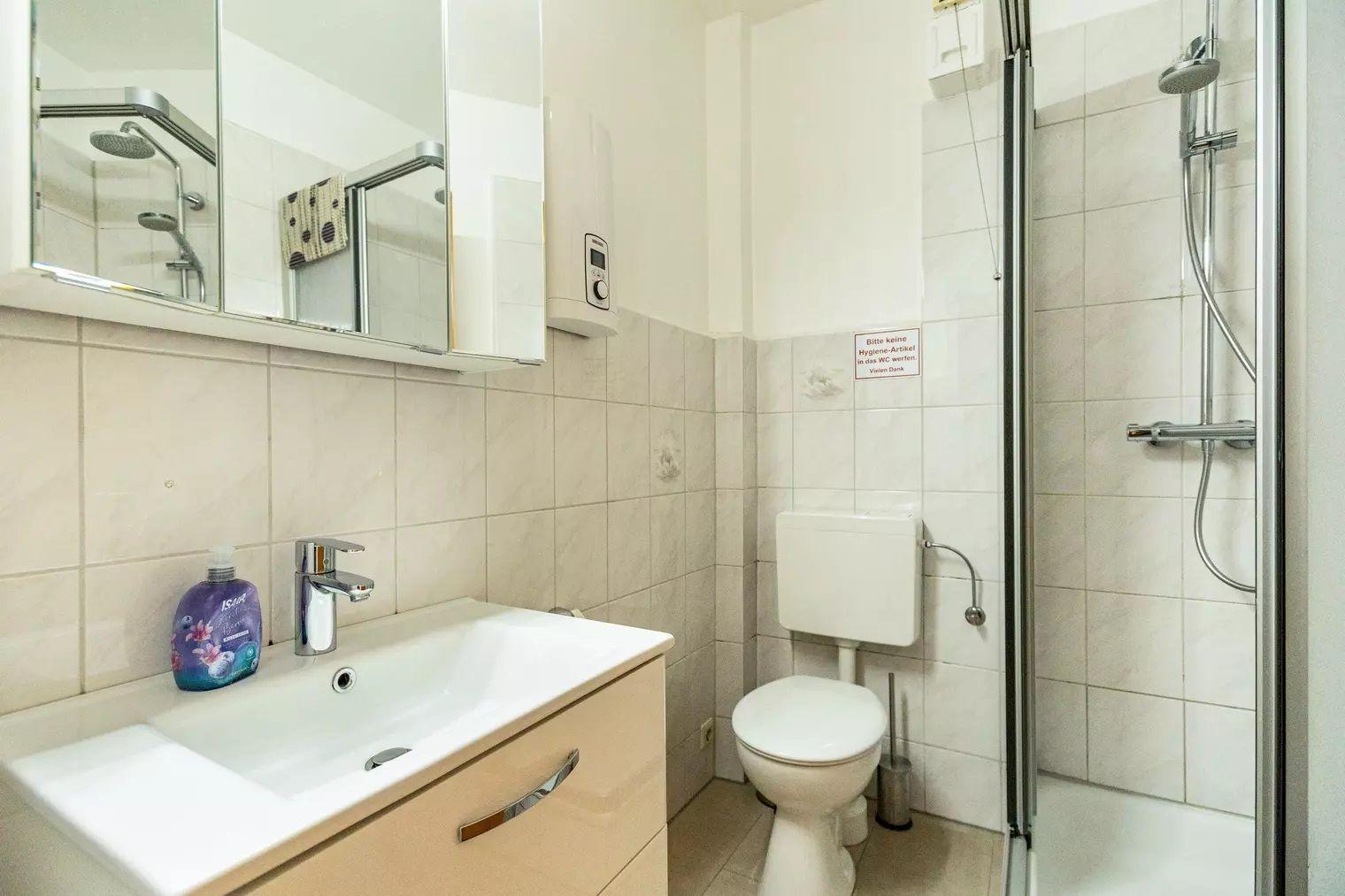 Badezimmer mit Dusche, Waschbecken und Toilette. Fliesenwand und Spiegelschrank.