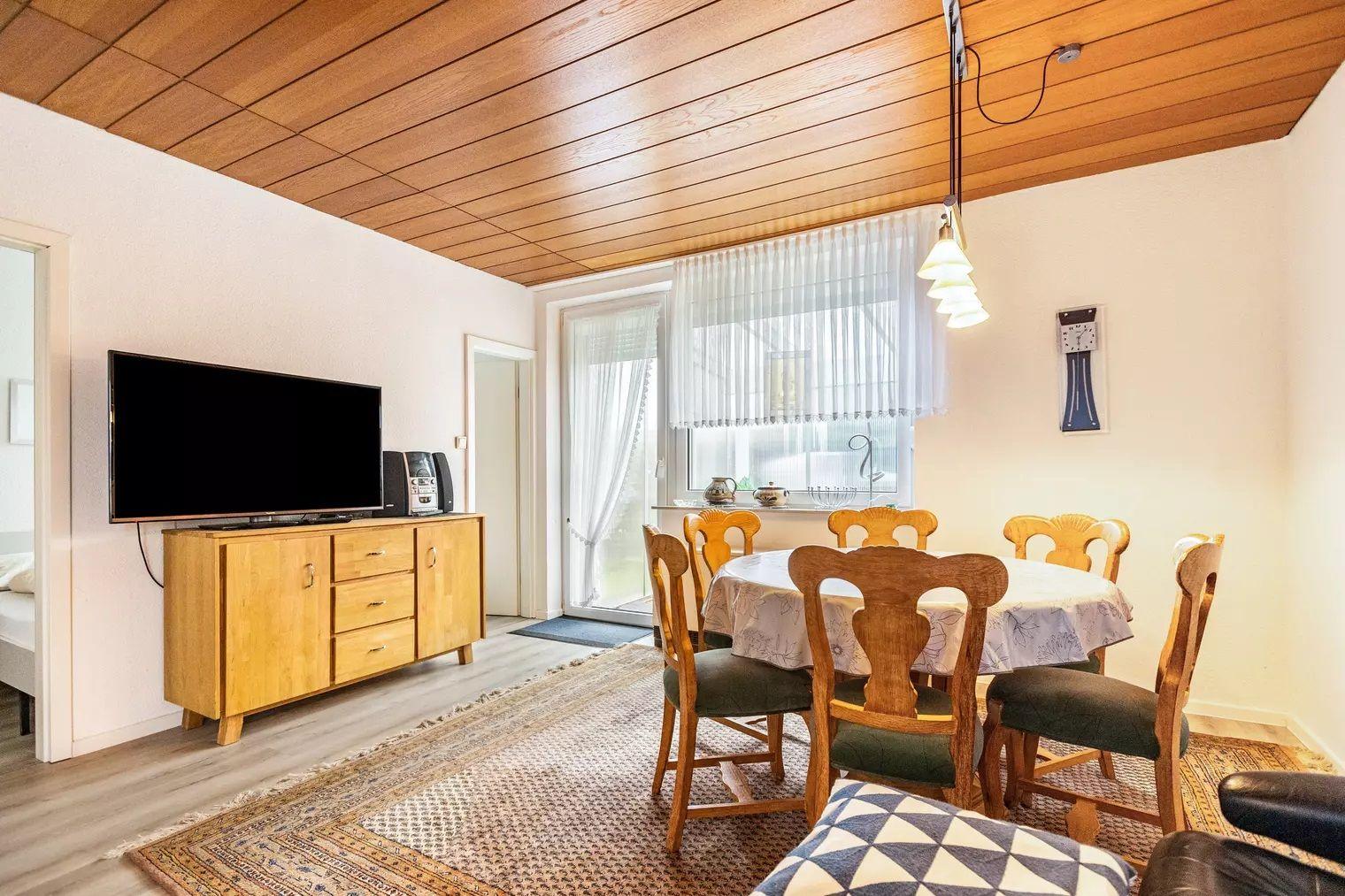 Wohn- und Essbereich mit Holzdecke, Esstisch, TV und Fenster.