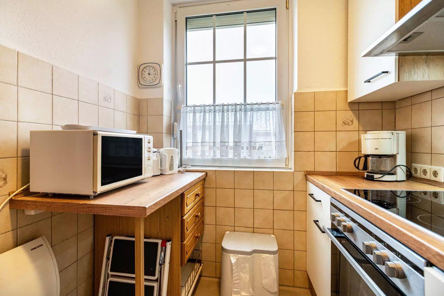 Küche mit Mikrowelle, Kaffeemaschine und Fenster mit Gardine.