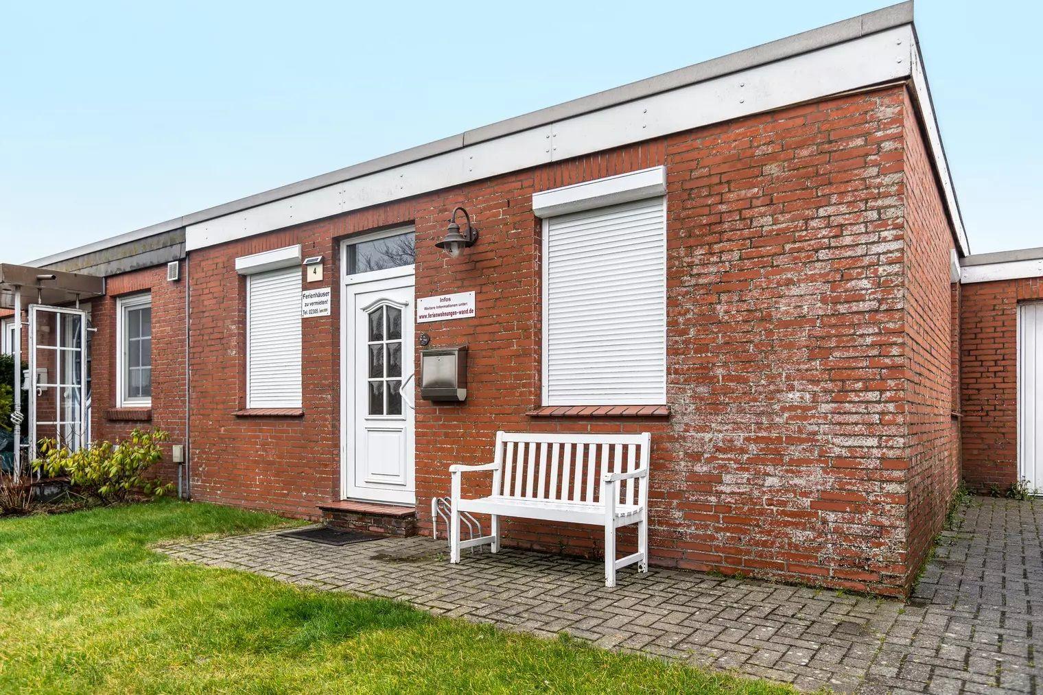 Rotes Backsteinhaus mit weißer Tür und Bank vorne.