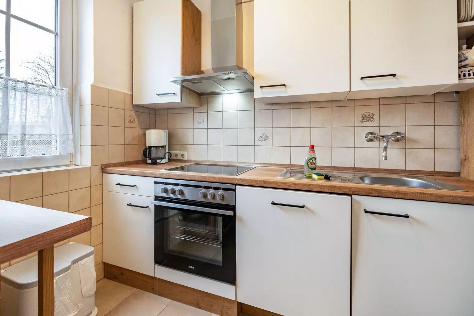 Küche mit weißen Schränken, Holzoberfläche und integriertem Ofen.