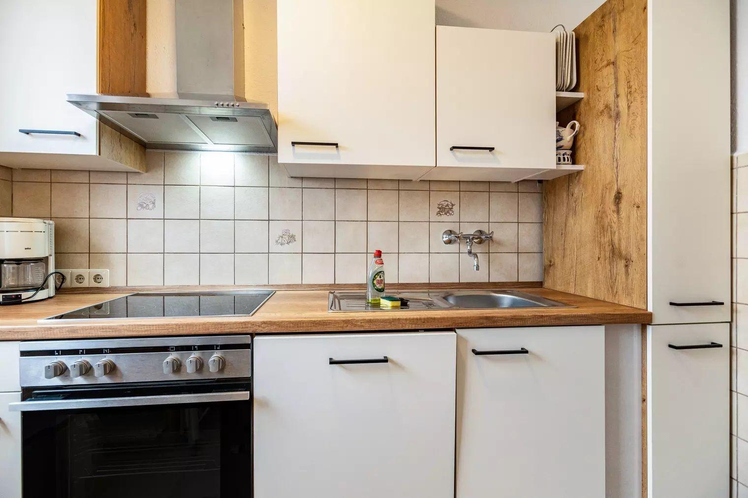 Küche mit weißen Schränken, Holzoberfläche und Edelstahlspüle.